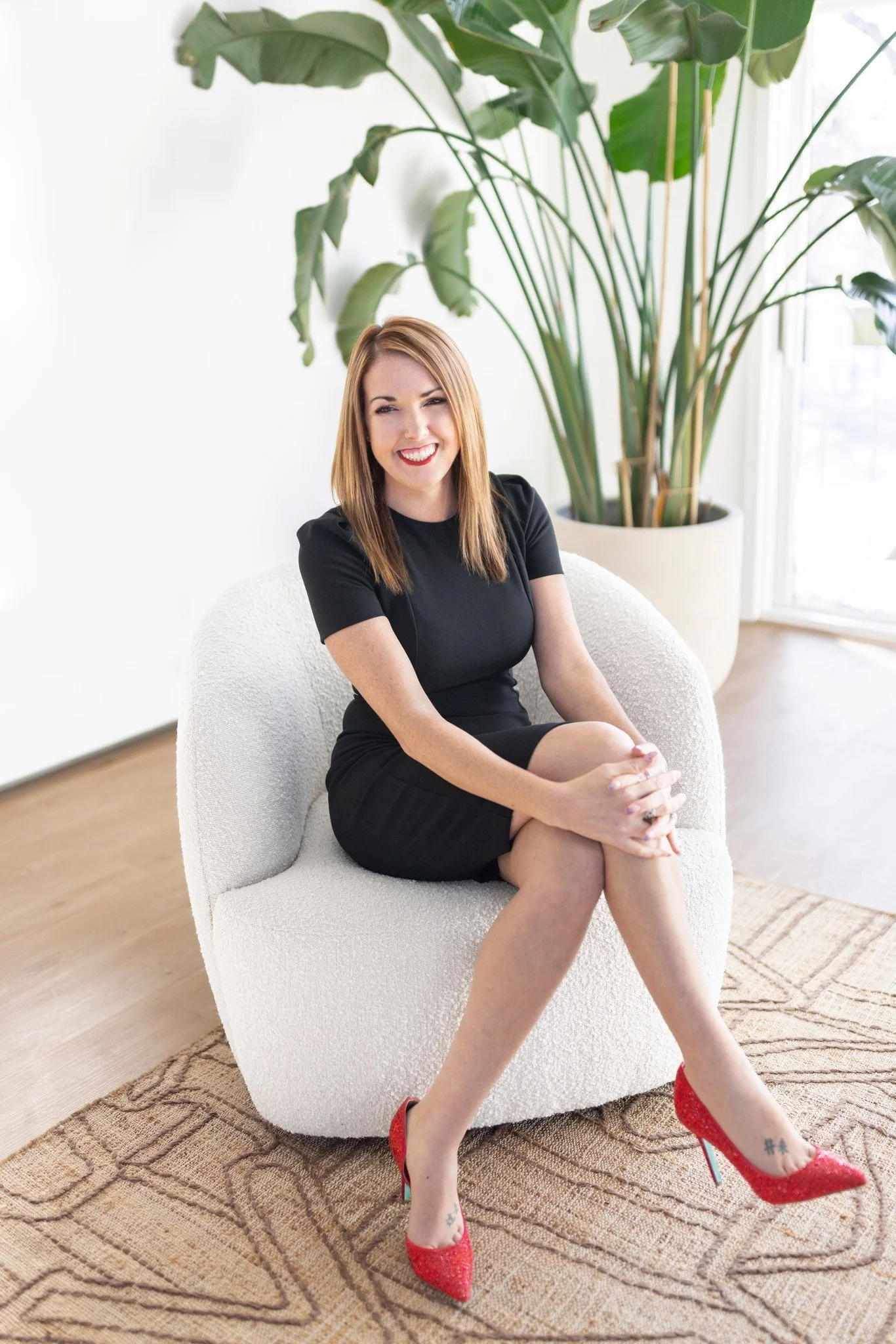 Realtor Nicolette Thomas sitting in a white chair, wearing red high heels and smiling