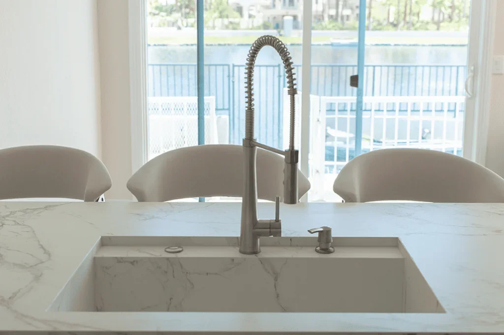 Modern kitchen island with a white marble countertop and a built-in sink, view of a sliding glass door with outdoor patio in the background.