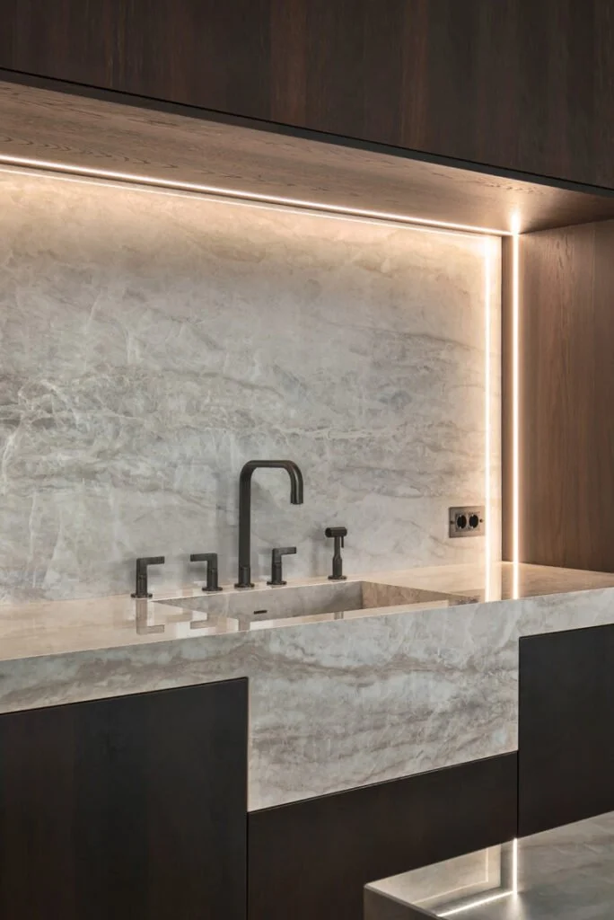 Minimalist kitchen with marble countertops and backsplash, black faucet and fixtures, and warm lighting along the edges.