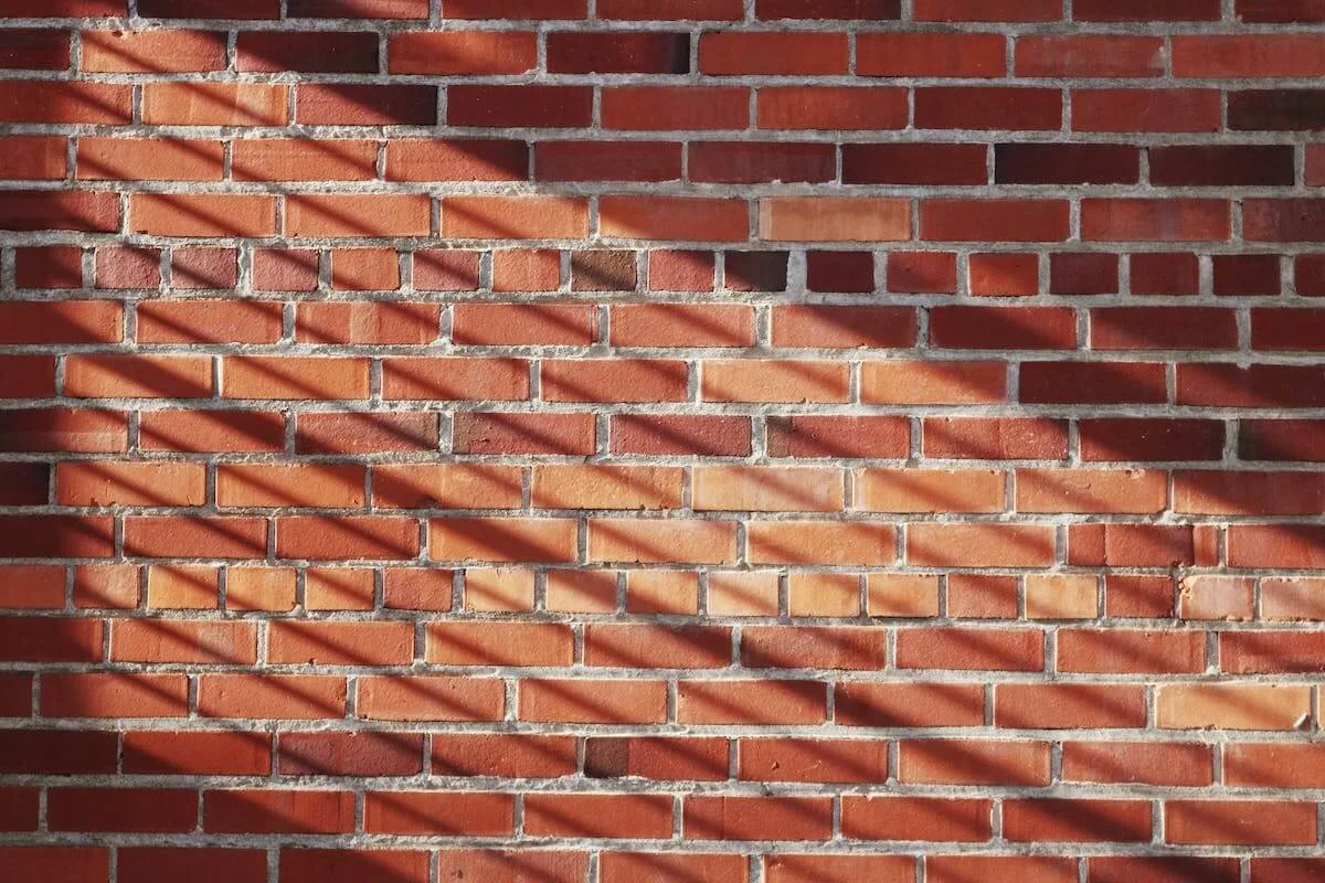 Sunlight and shadow cast by a nearby object across a red brick wall.