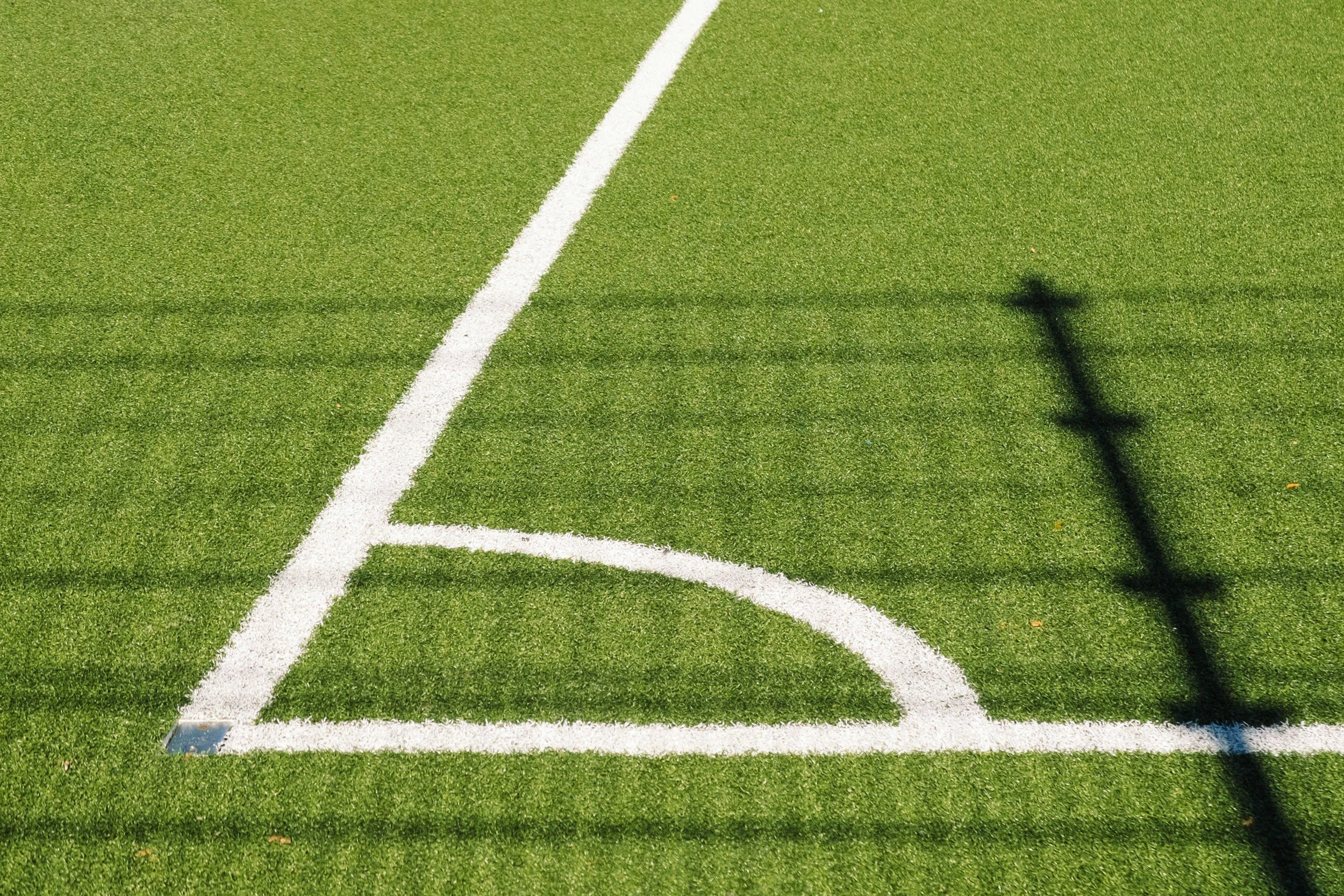A green sports field with white lines and a shadow of a light pole.