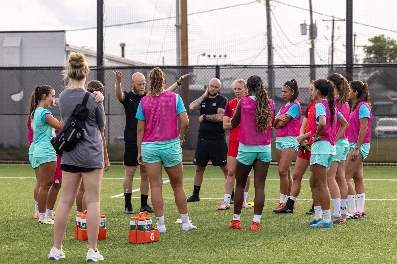 Women's soccer team during a training session on the field, listening to their coaches.