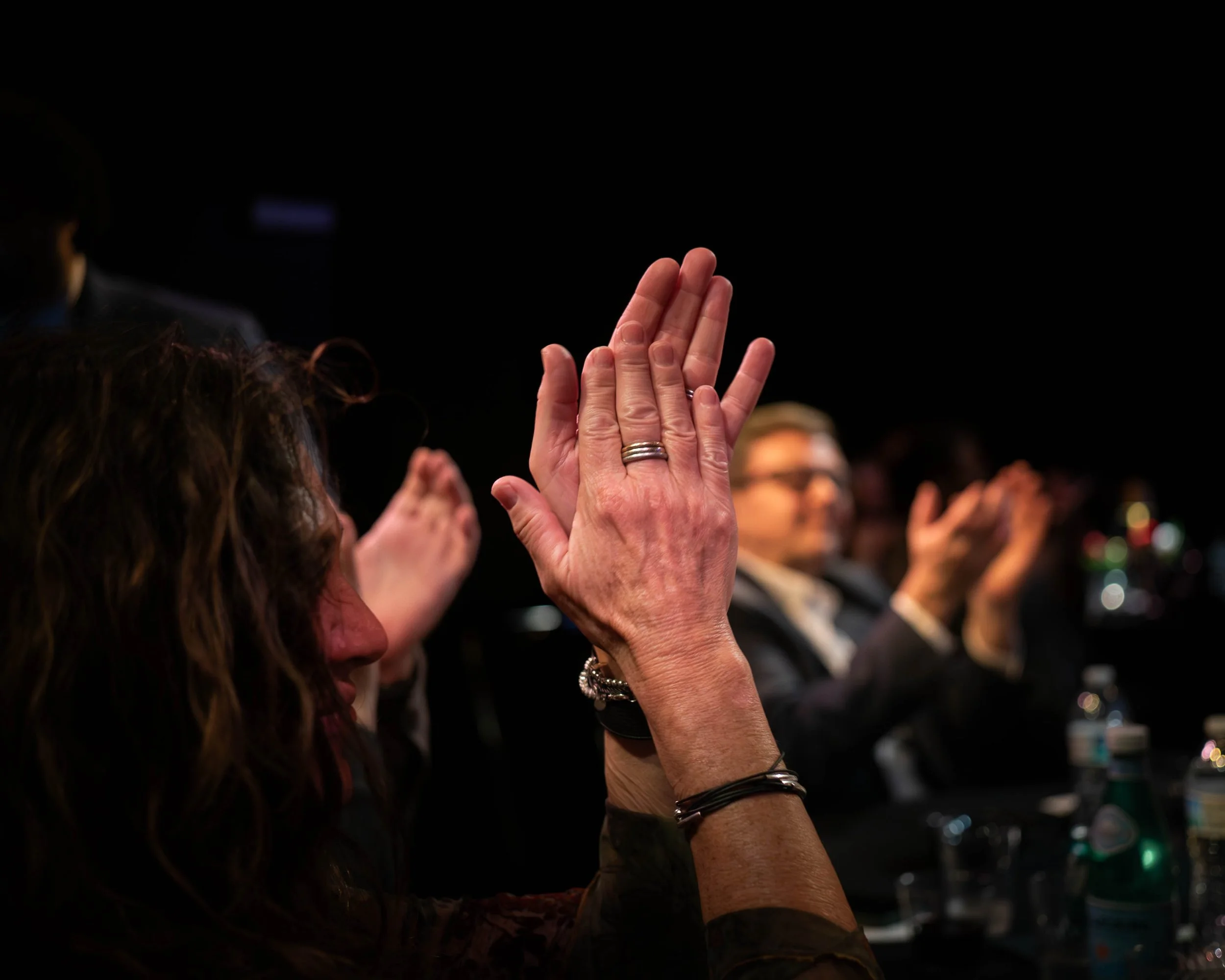 People at a conference or meeting applauding, with a focus on a woman's hands clapping.