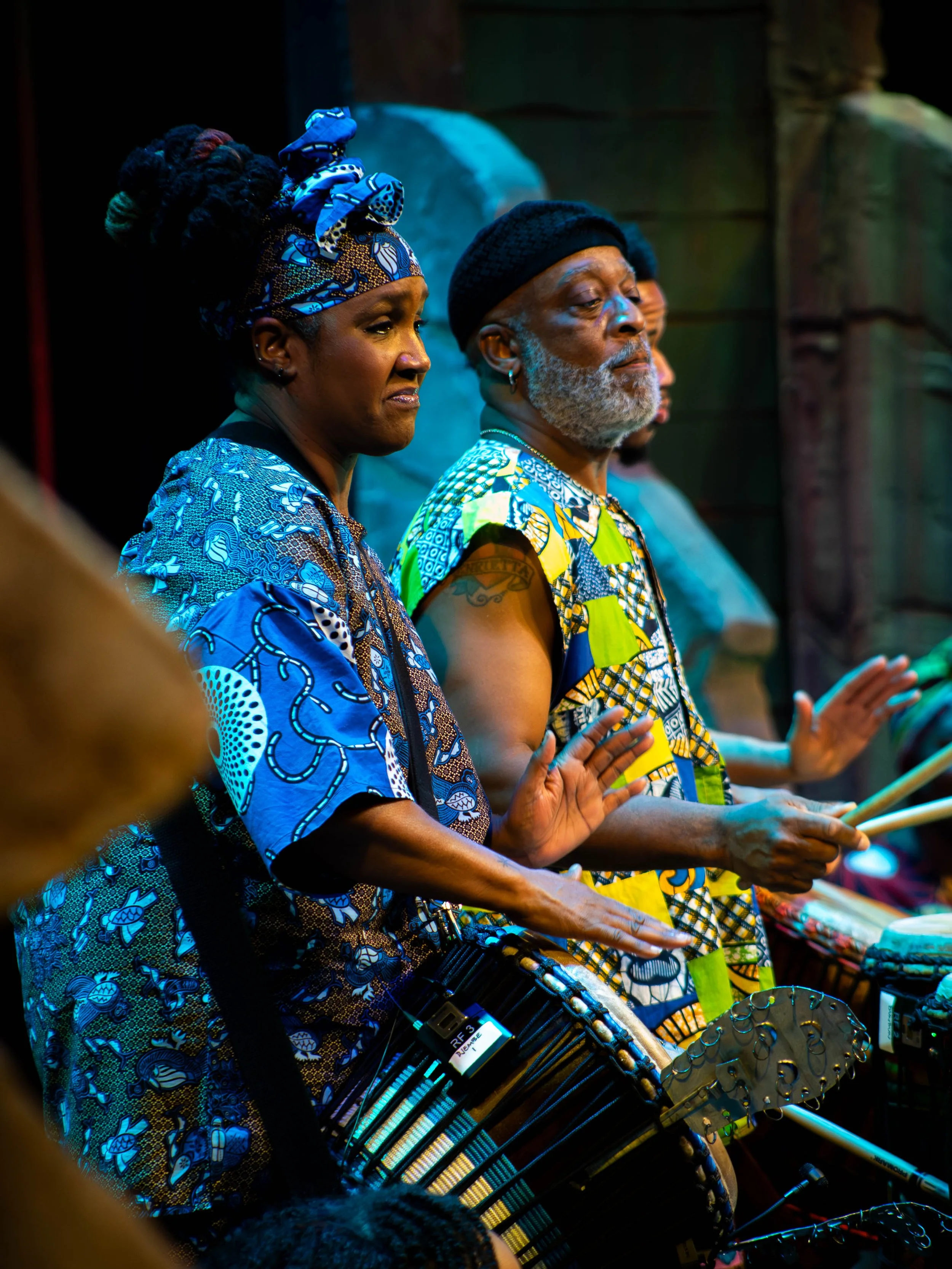 Musicians playing drums in traditional African attire during a performance.
