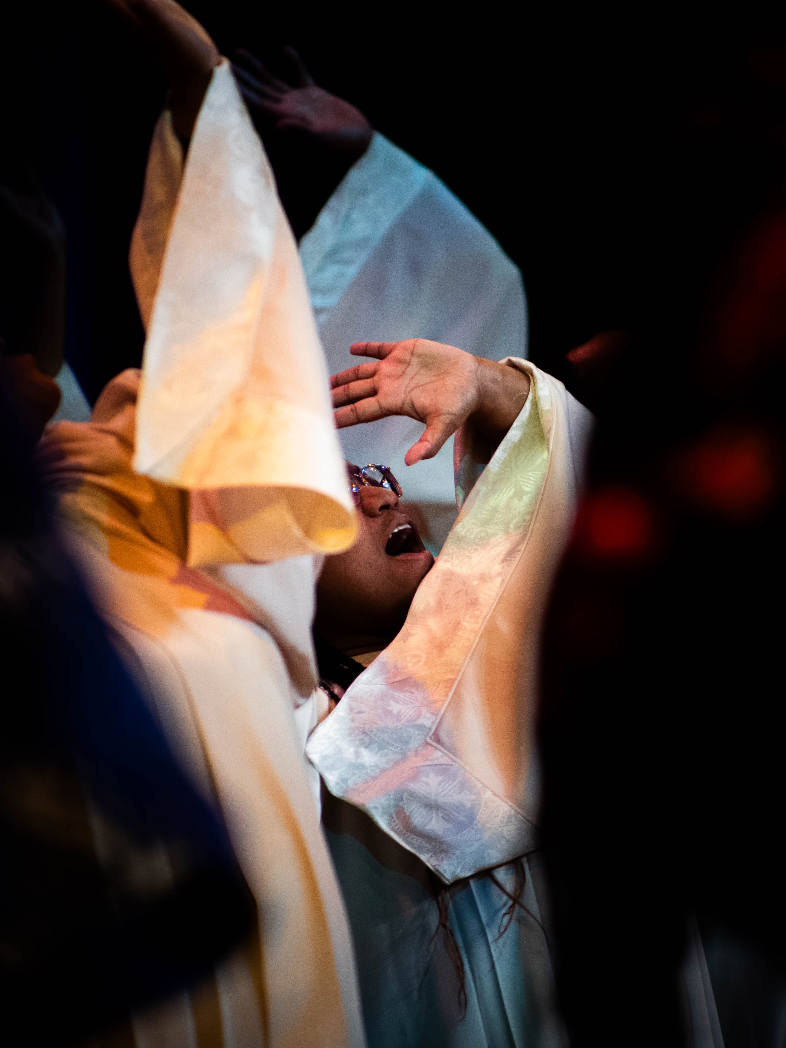 A person dressed in a graduation gown is being overwhelmed with emotion during a graduation ceremony, with their hand raised to their forehead and their mouth open.