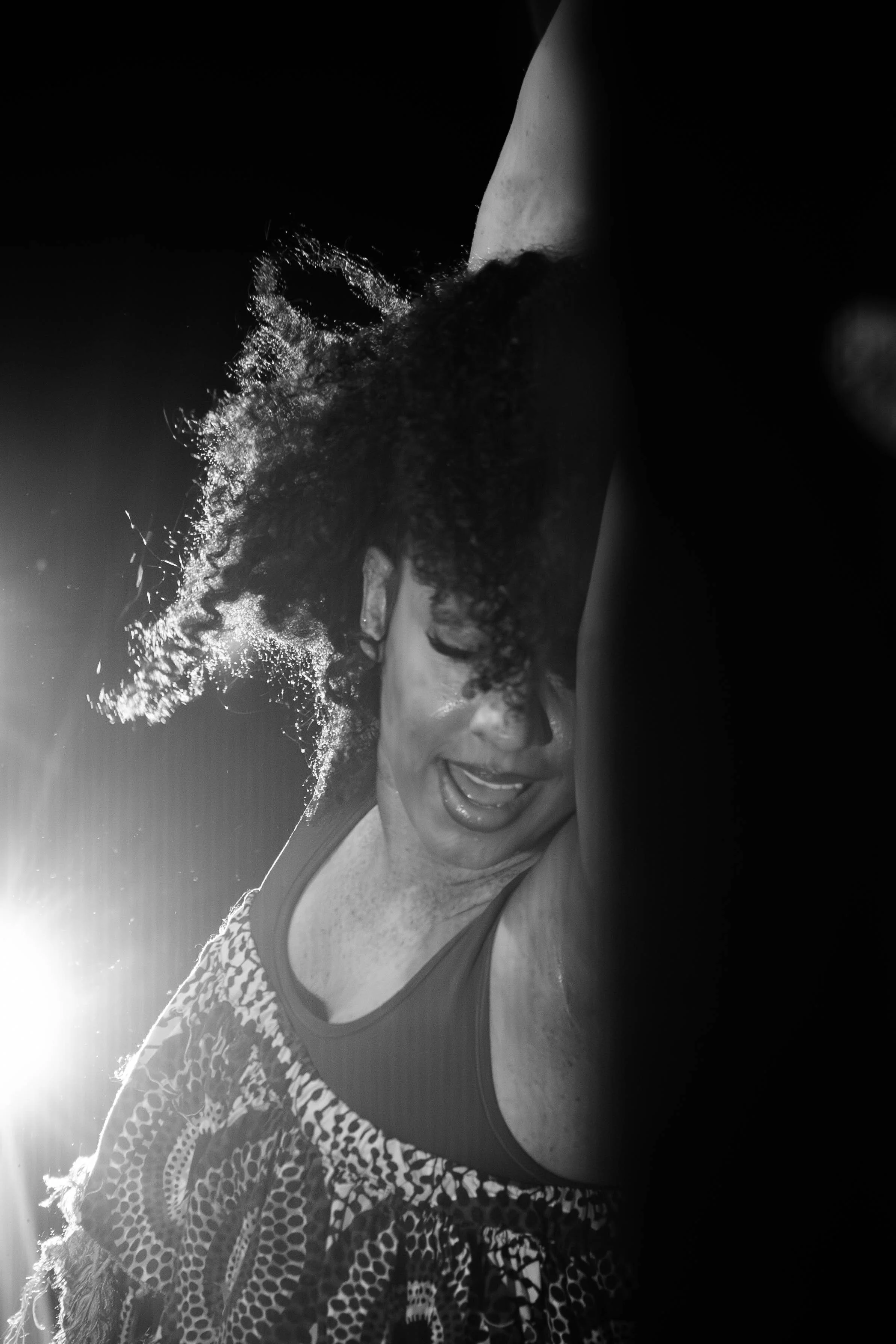 A woman with curly hair dancing or performing with her eyes closed, wearing a patterned top, in a dramatic lighting setting.
