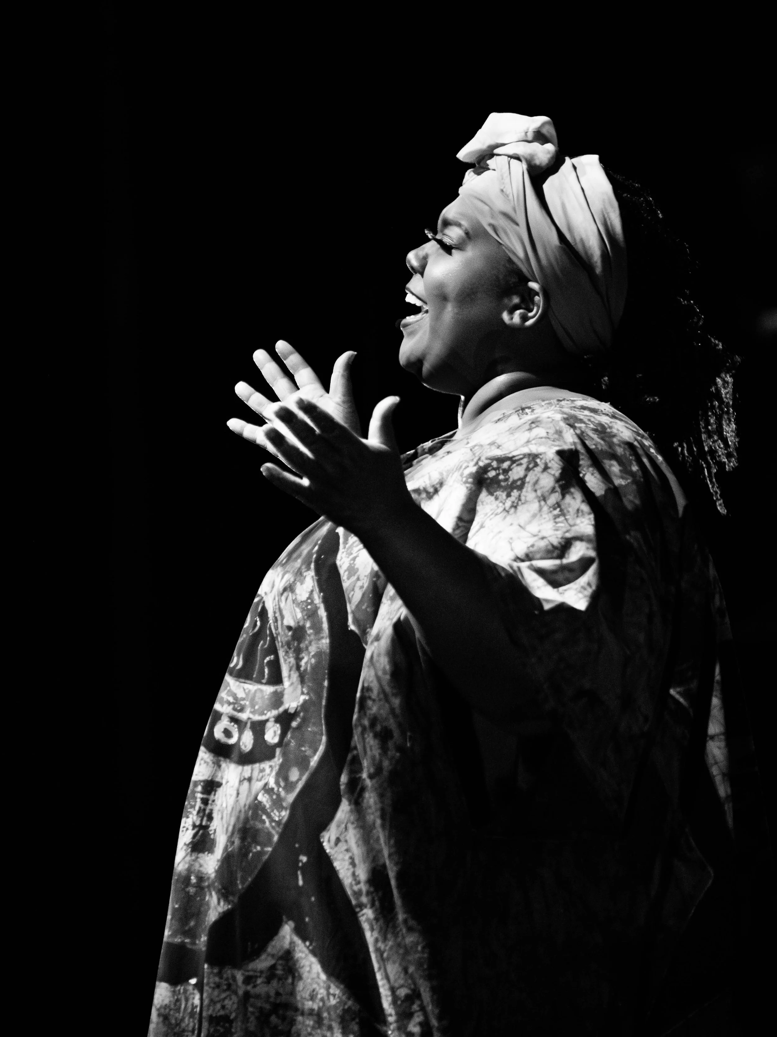 A woman with a headscarf smiling and clapping in black and white.