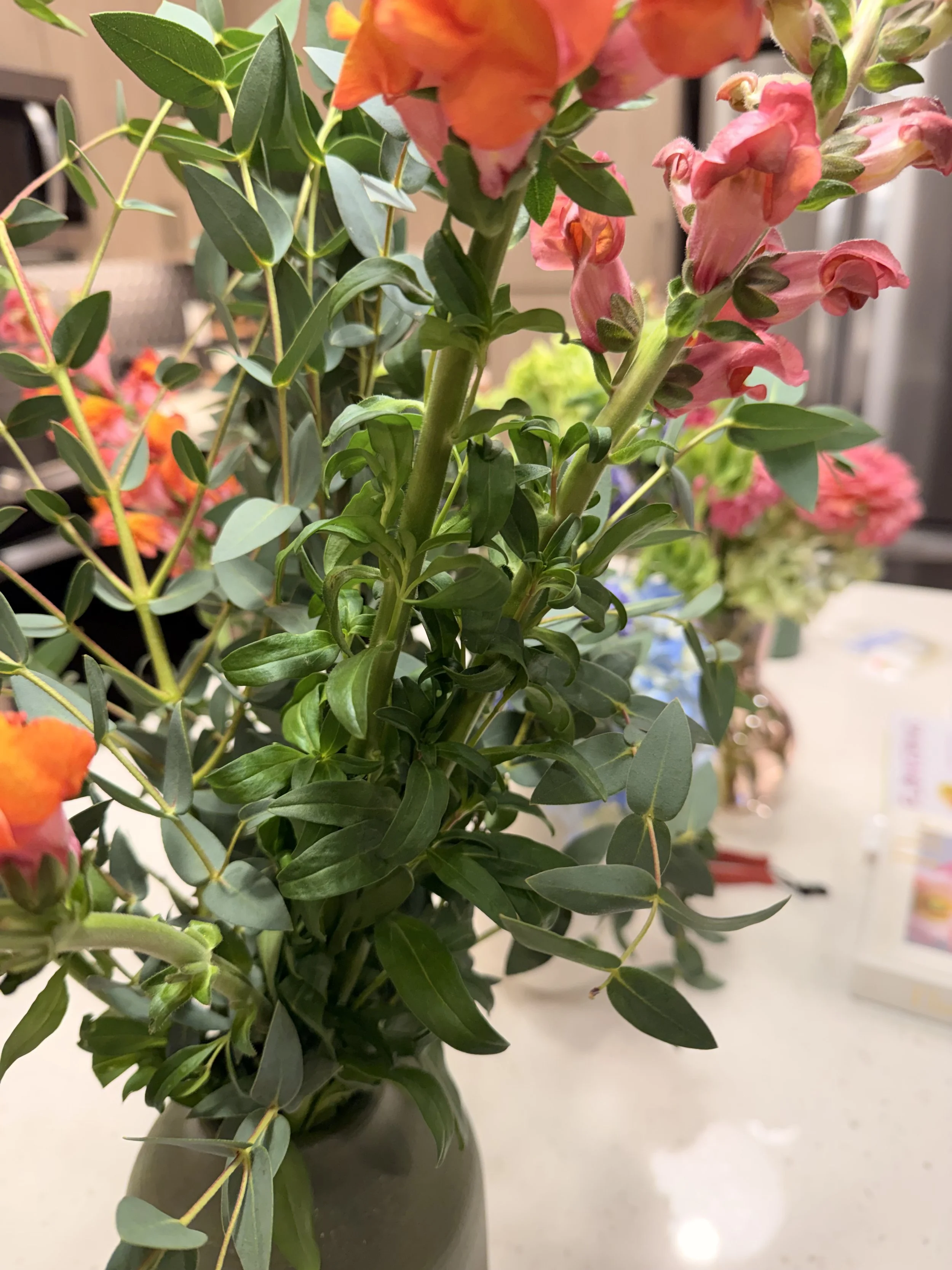 Close-up of a colorful flower arrangement in a black vase, featuring pink, orange, and green flowers and foliage on a table.