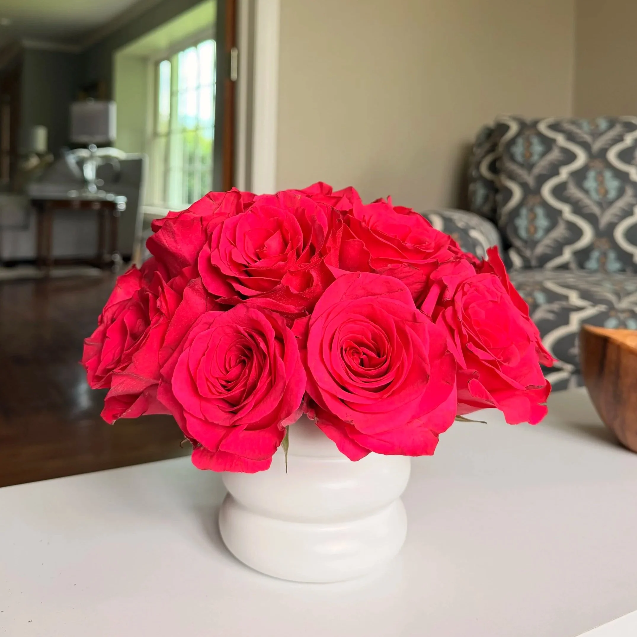A bouquet of red flowers in a white vase placed on a white surface.