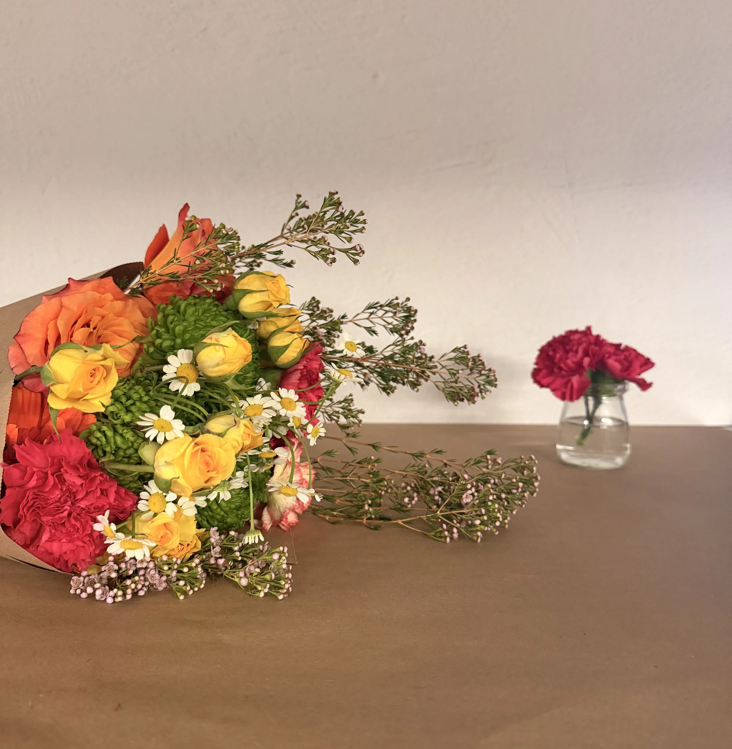 A bouquet of pink, orange, and green flowers wrapped in brown paper rests on a white countertop.