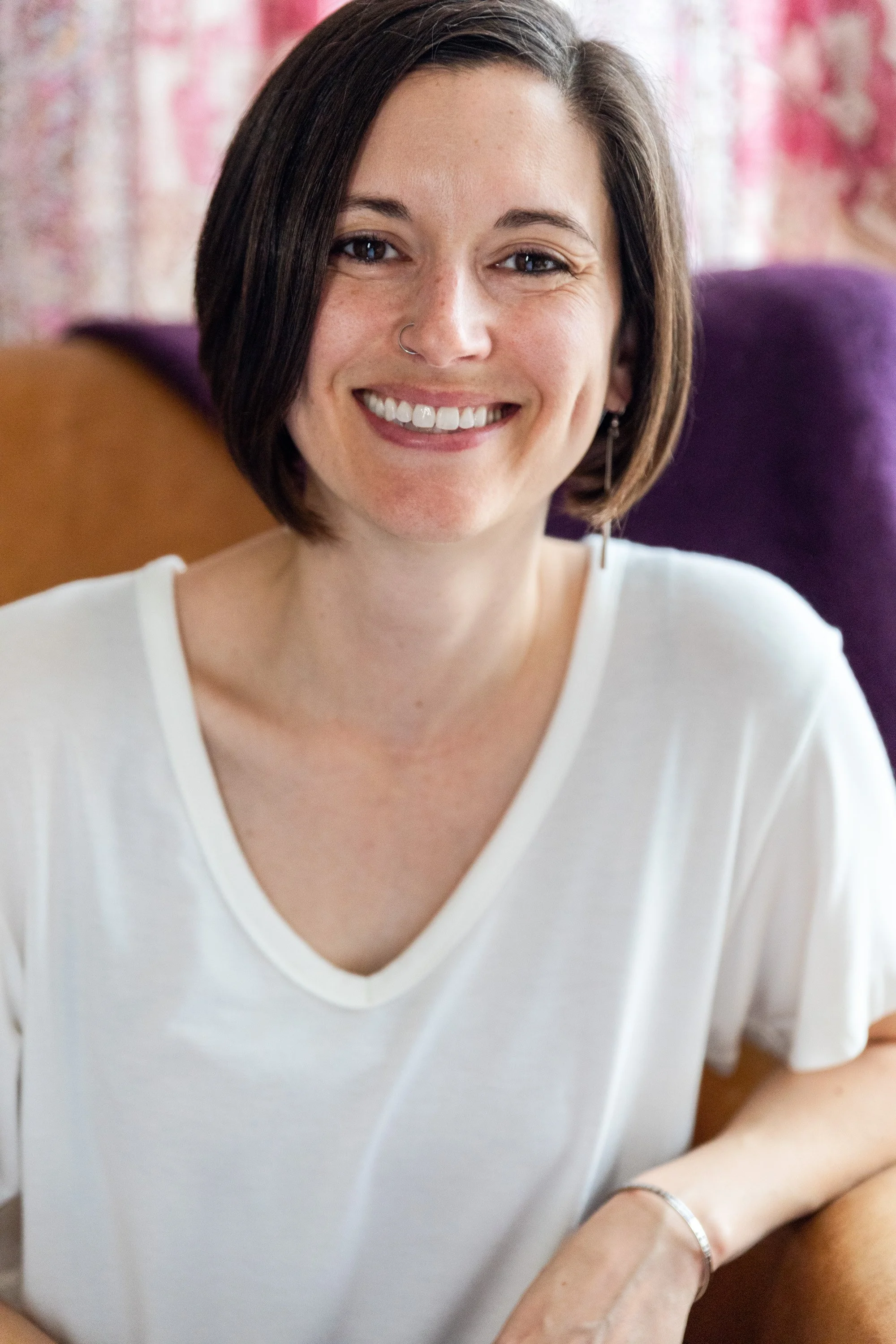 A portrait image of Elyse Robertson, a white woman with short, dark brown hair. She is wearing a white t-shirt, smiling and looking at the camera.