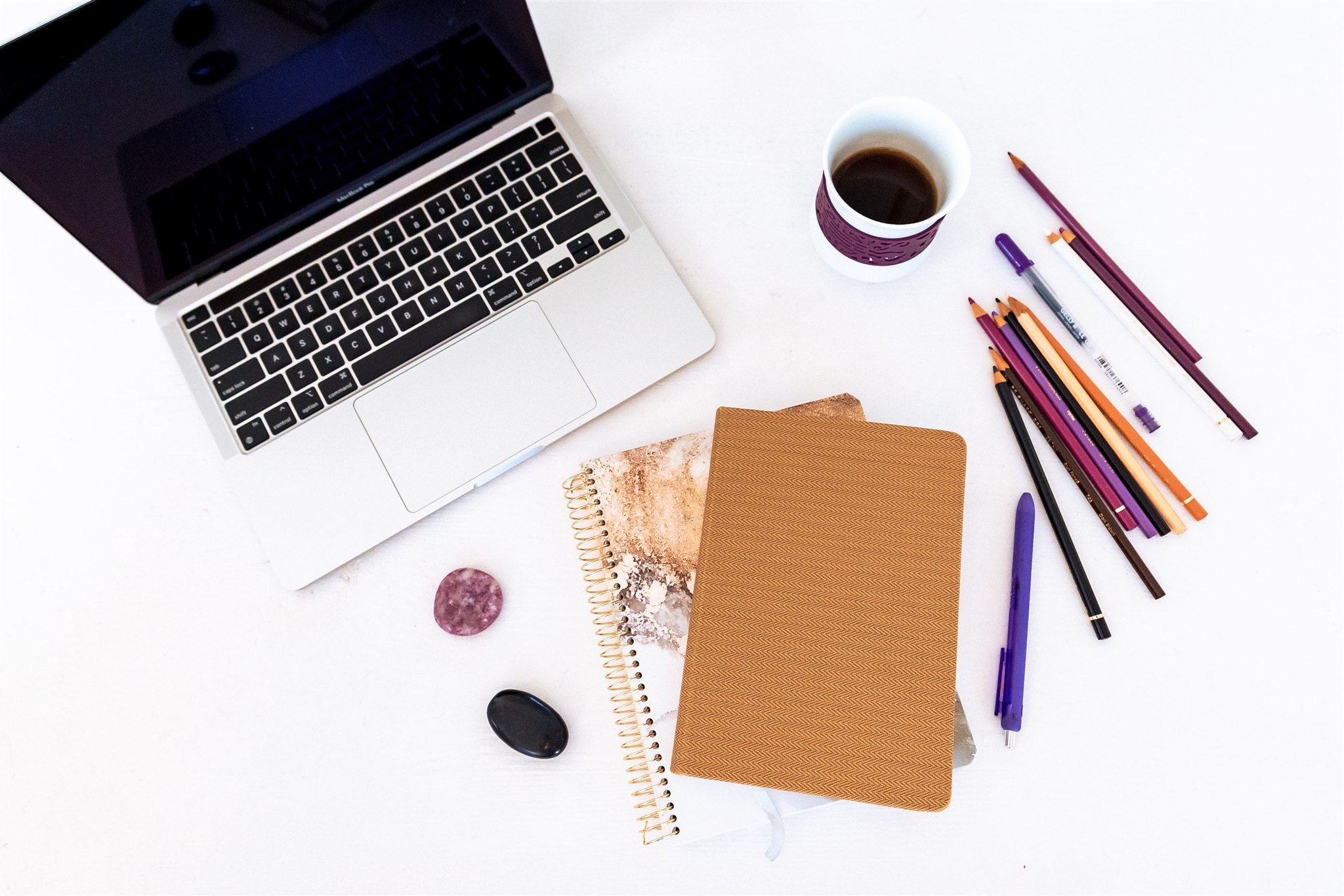 A overhead view of an open laptop computer, two stacked notebooks, and a purple and black stone