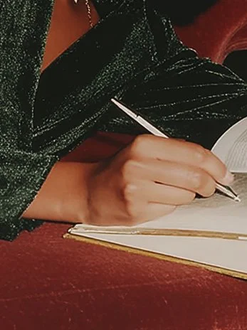 A person writing on a notepad with a pen, wearing a dark, sparkly dress.