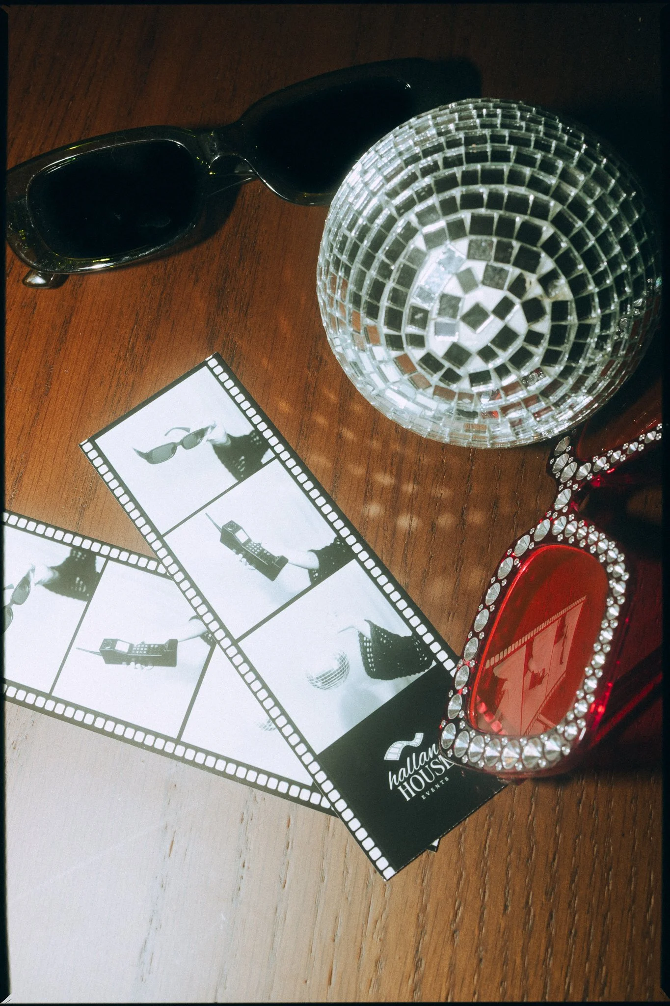 A wooden table with black sunglasses, a crystal disco ball, a small red item decorated with rhinestones, a black and white photo strip, and a bride and groom wedding scene with the text 'Nadlam House Events'.