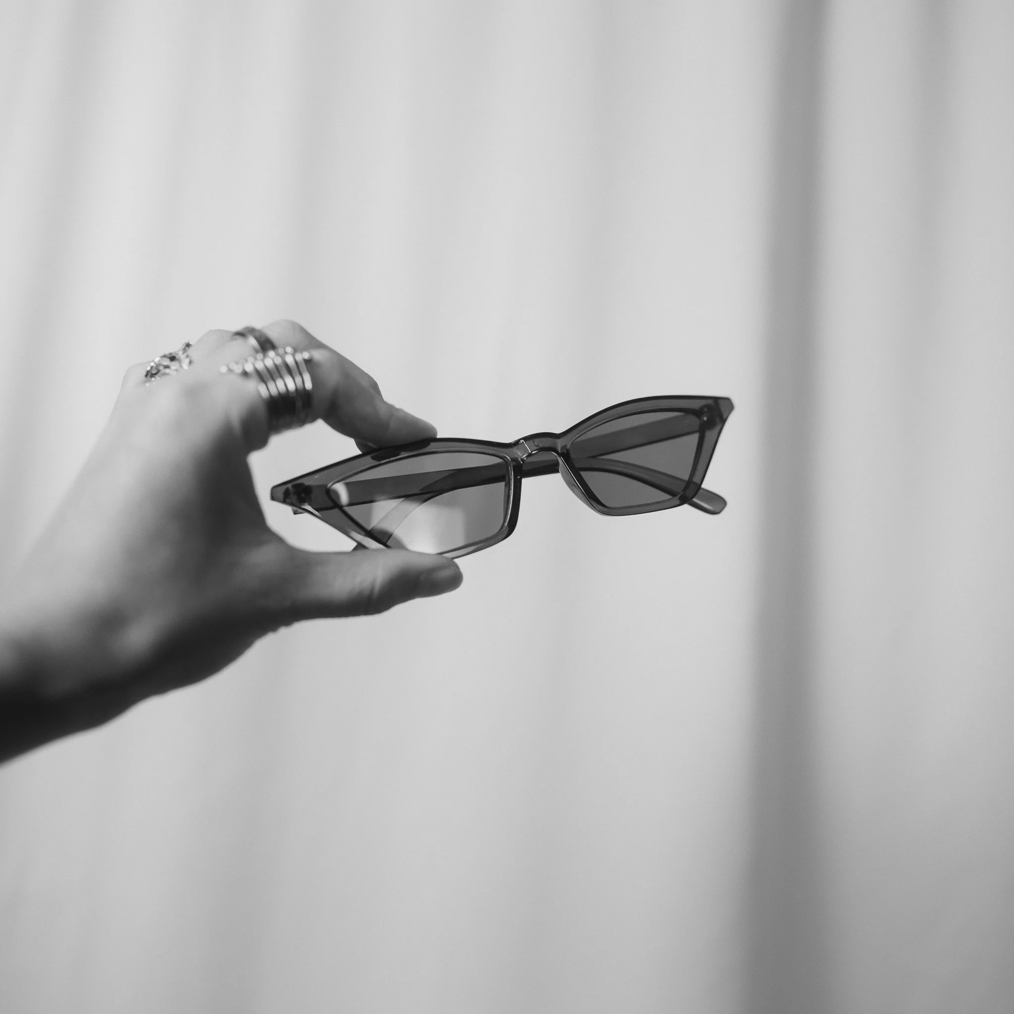 A hand holding a pair of black sunglasses with a blurred background