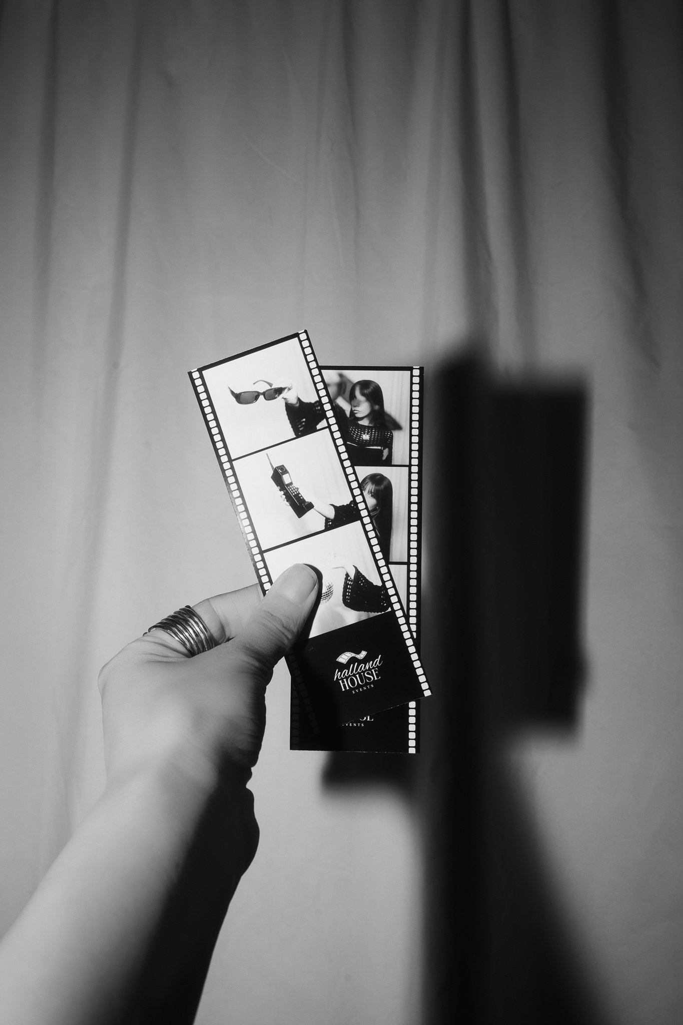A hand holding two photo booth strips with images of a woman modeling accessories against a plain background.