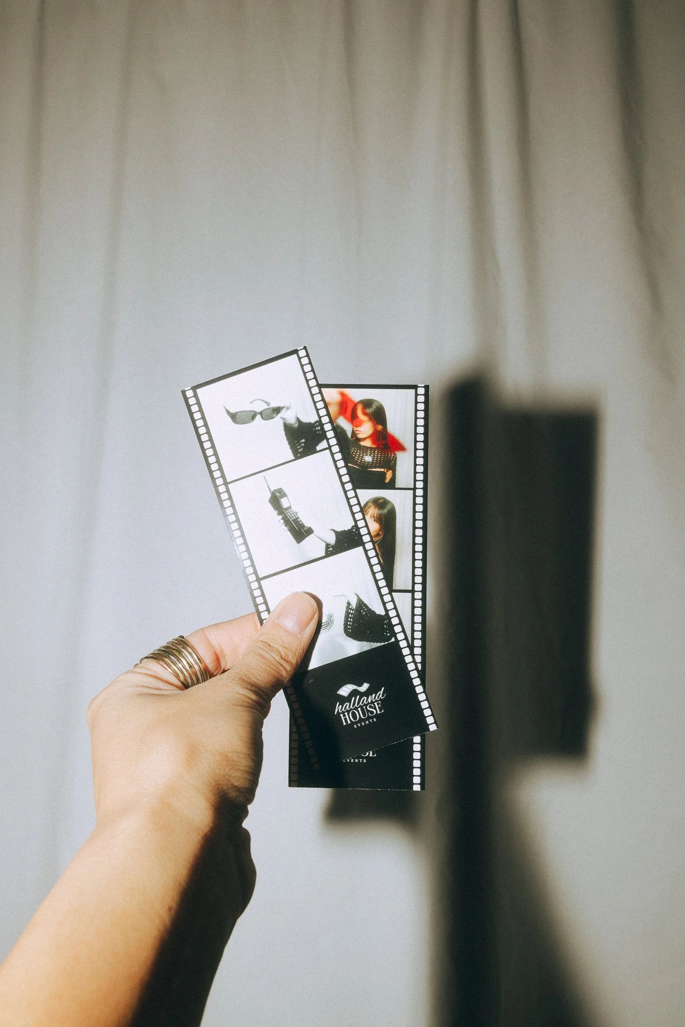 Two photo booth strips held in hand, featuring images of people and items, with a plain, light-colored wall in the background.