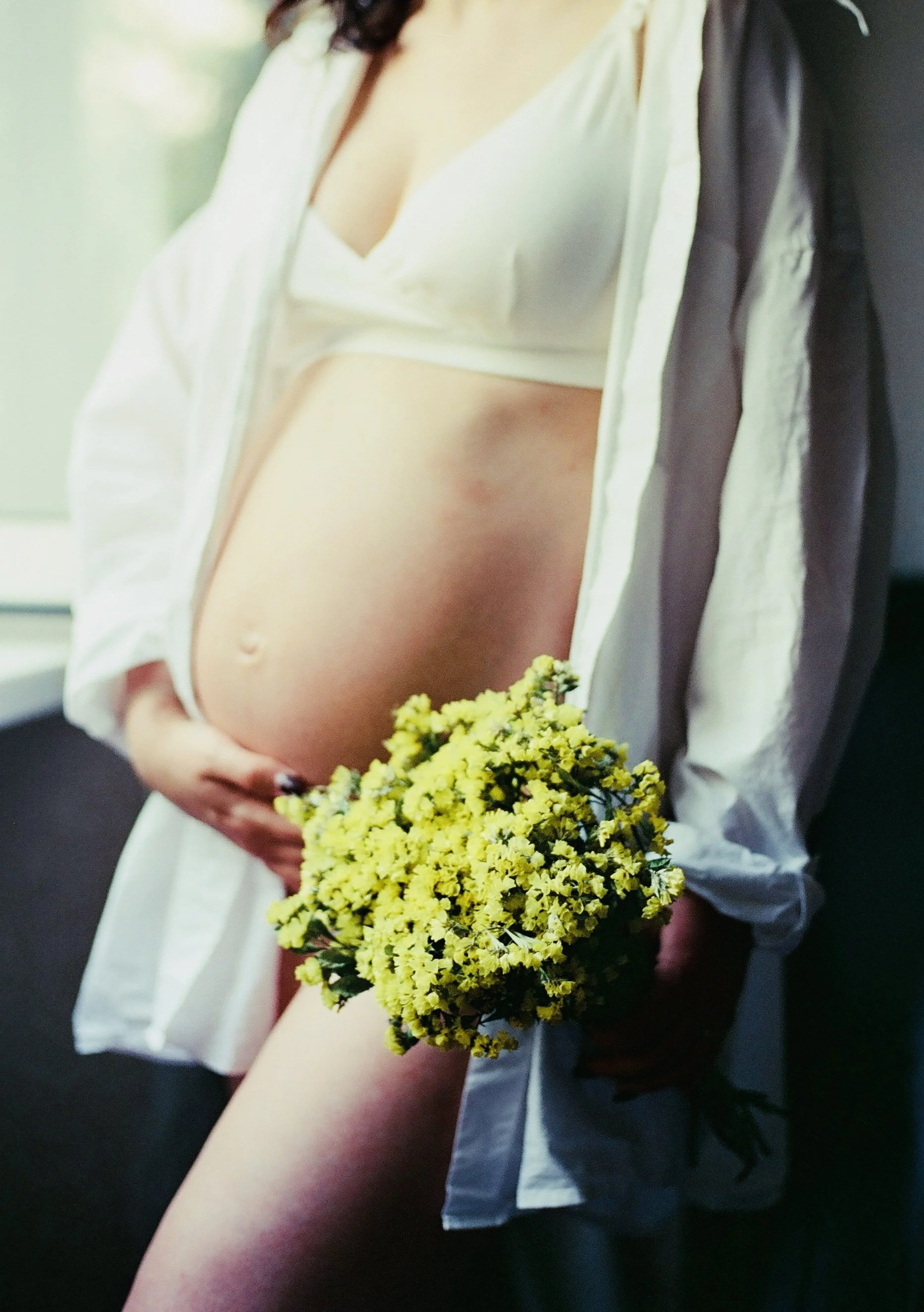 A woman in a white top and gray shirt holding a bouquet of small yellow flowers.