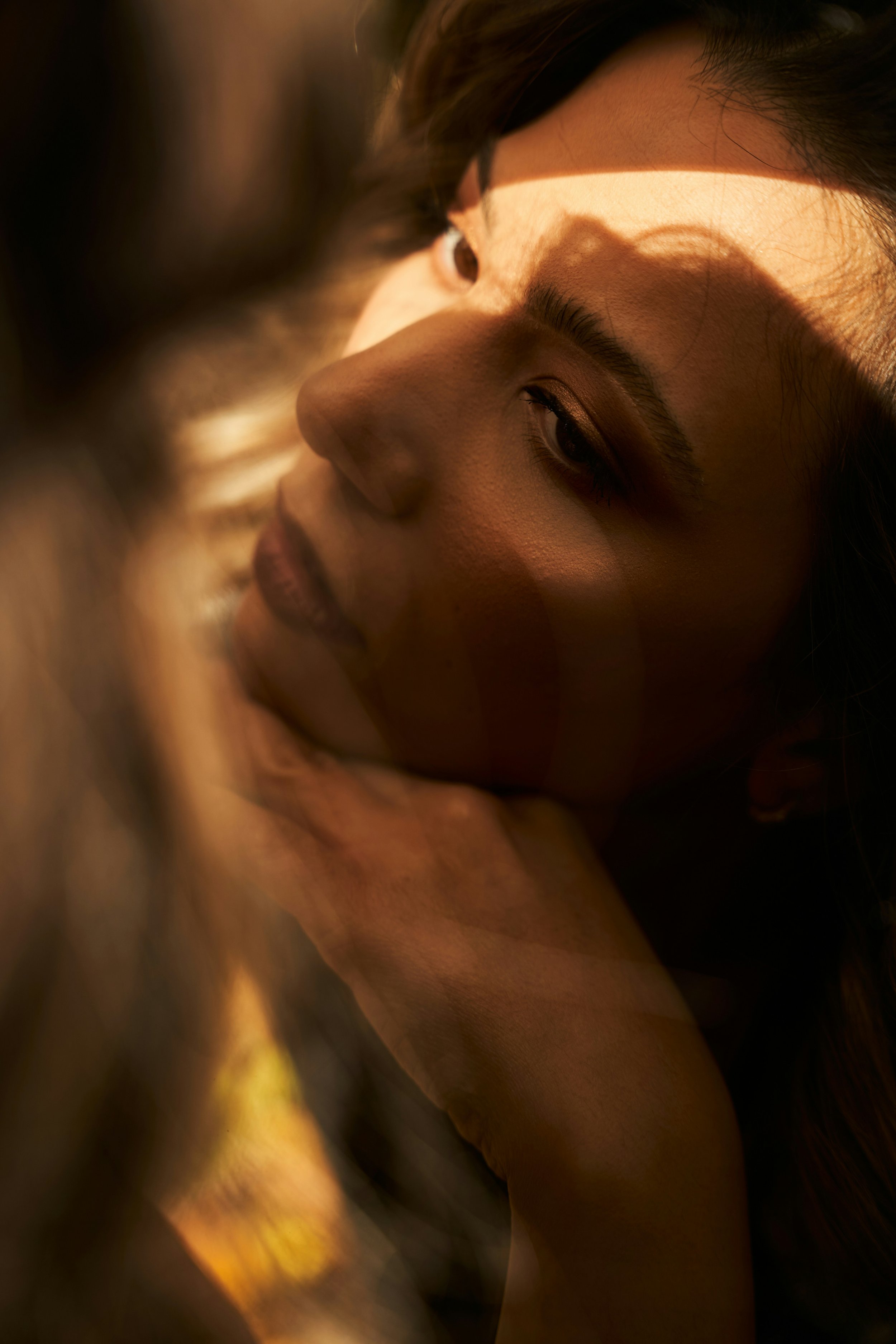 Close-up of a woman's face with warm lighting, showing her eye, eyebrow, and part of her nose and lips, with shadows cast on her face.
