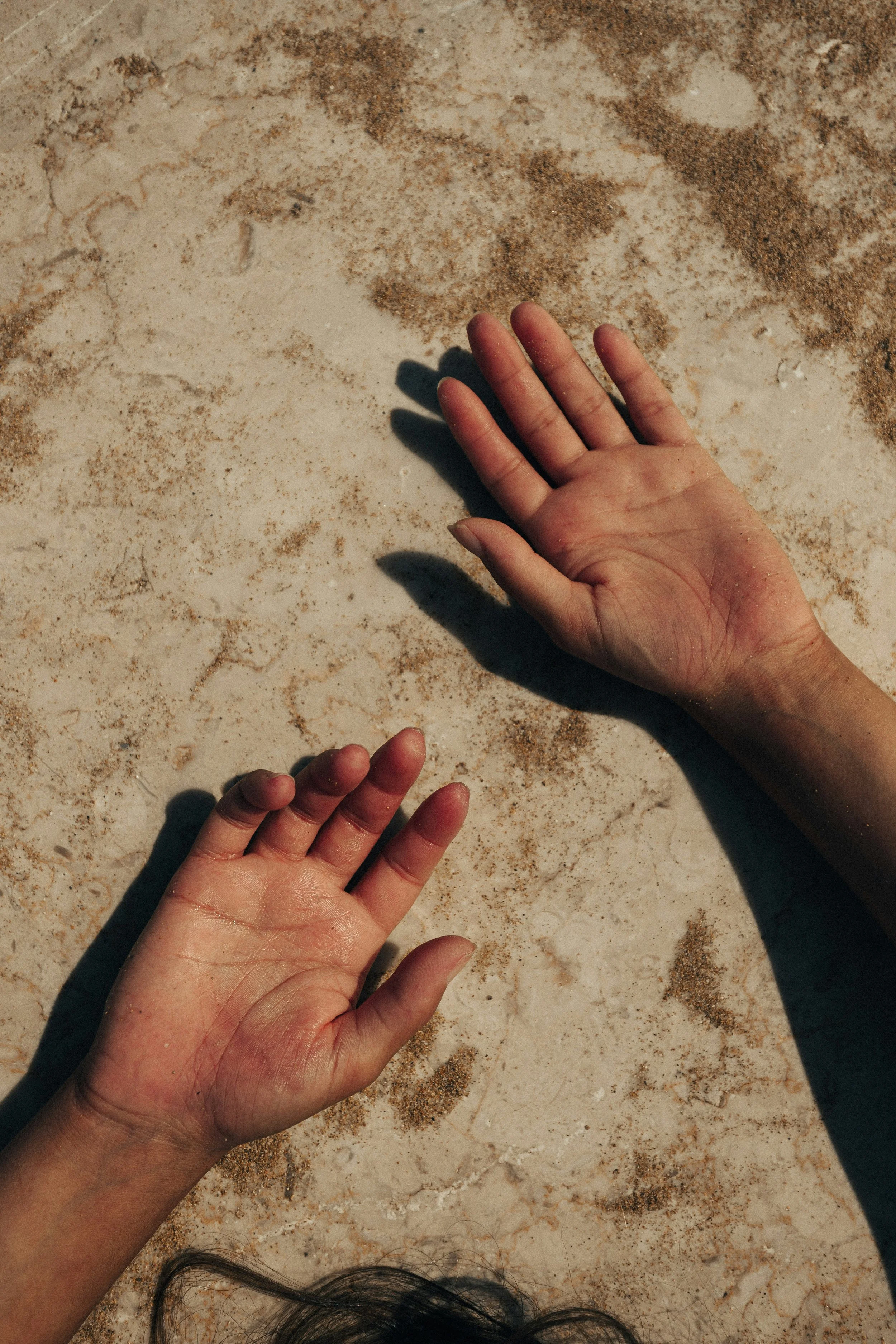 Two hands, one adult and one child's, reaching towards each other on a sandy surface.