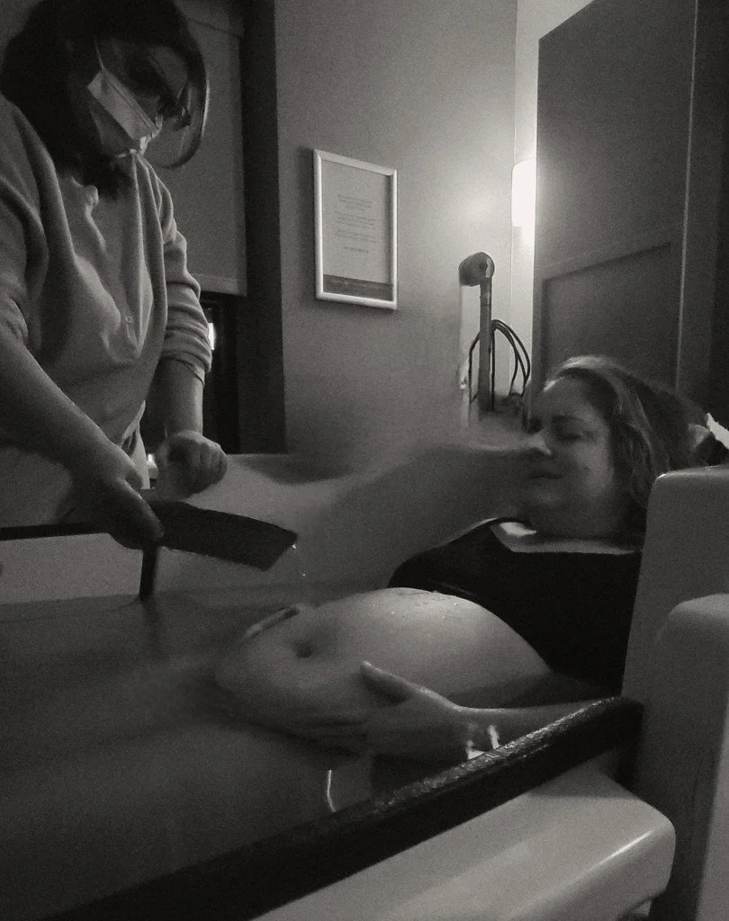 A woman receiving a pregnancy ultrasound scan in a medical office, with a healthcare professional holding the ultrasound device.