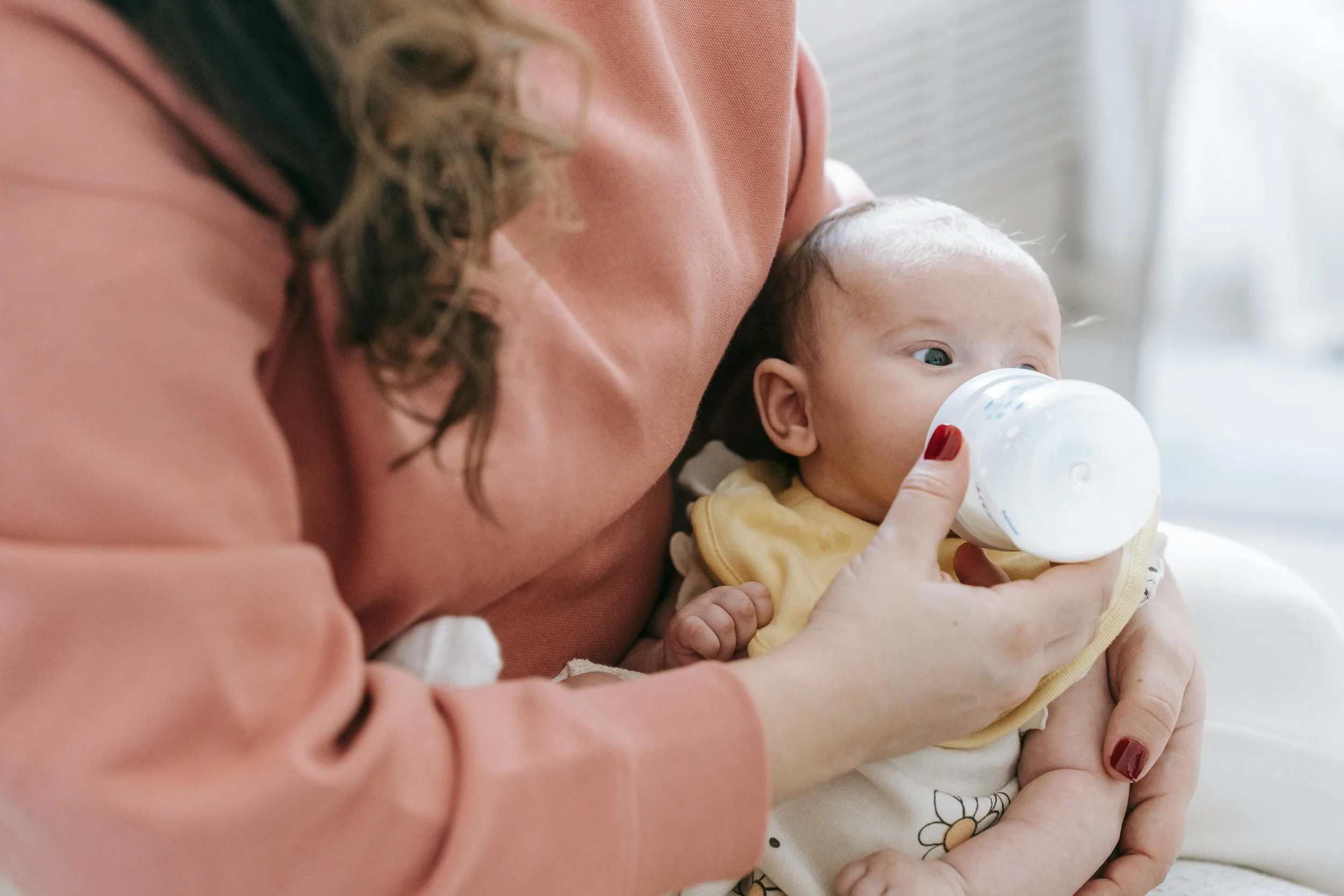 Woman trying to bottle feed a baby. Overwhelmed and exhausted during postpartum, running on just a few hours of sleep and googling at 2 am if "this is normal" with her baby wishing she had a night nurse