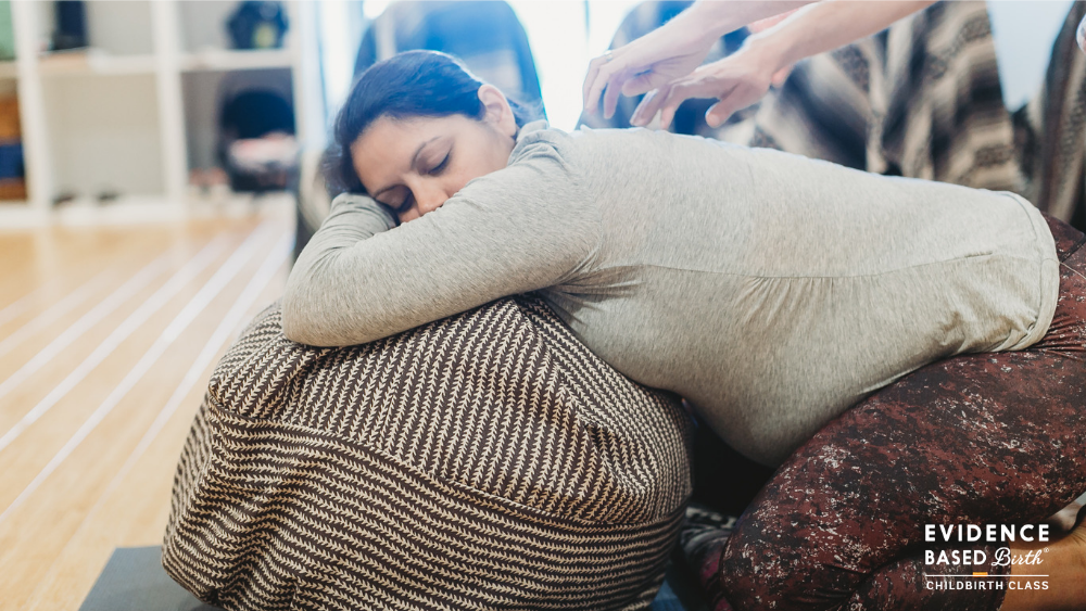 A woman lying on her side on a therapy ball with her eyes closed, receiving a chiropractic adjustment from a practitioner.
