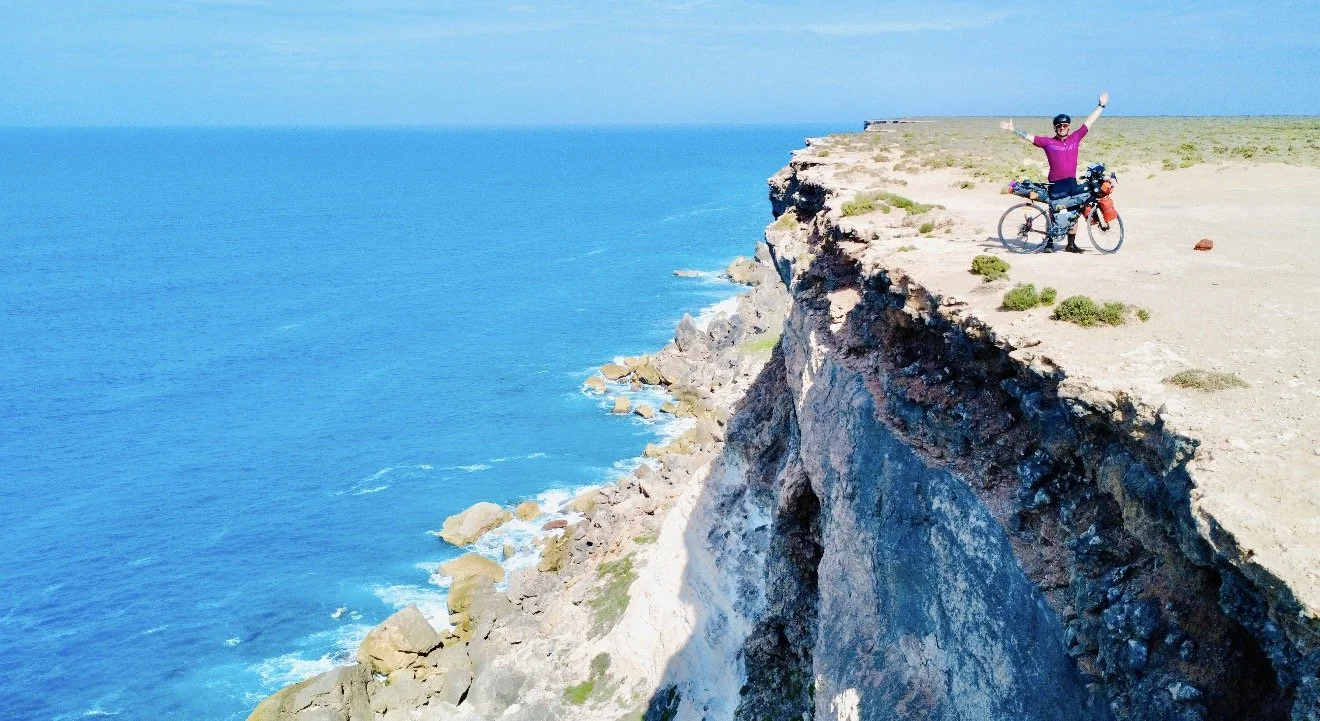 Matt with his touring bike above coastal cliffs and a bright blue ocean