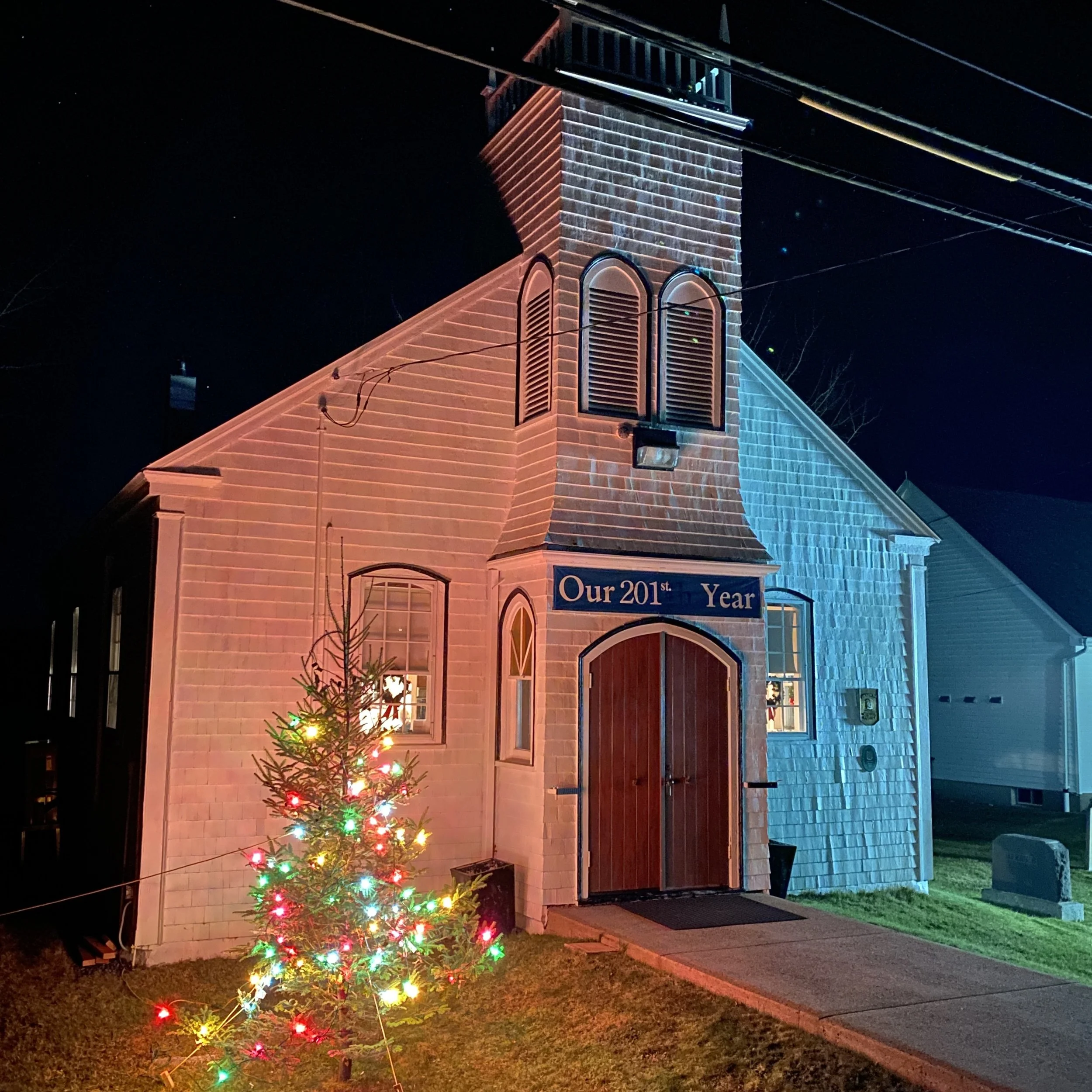 At night a Charlie Brown tree decorated with multi coloured lights stands in front of the church in memory of special friends and family. Light shines from the sanctuary windows.