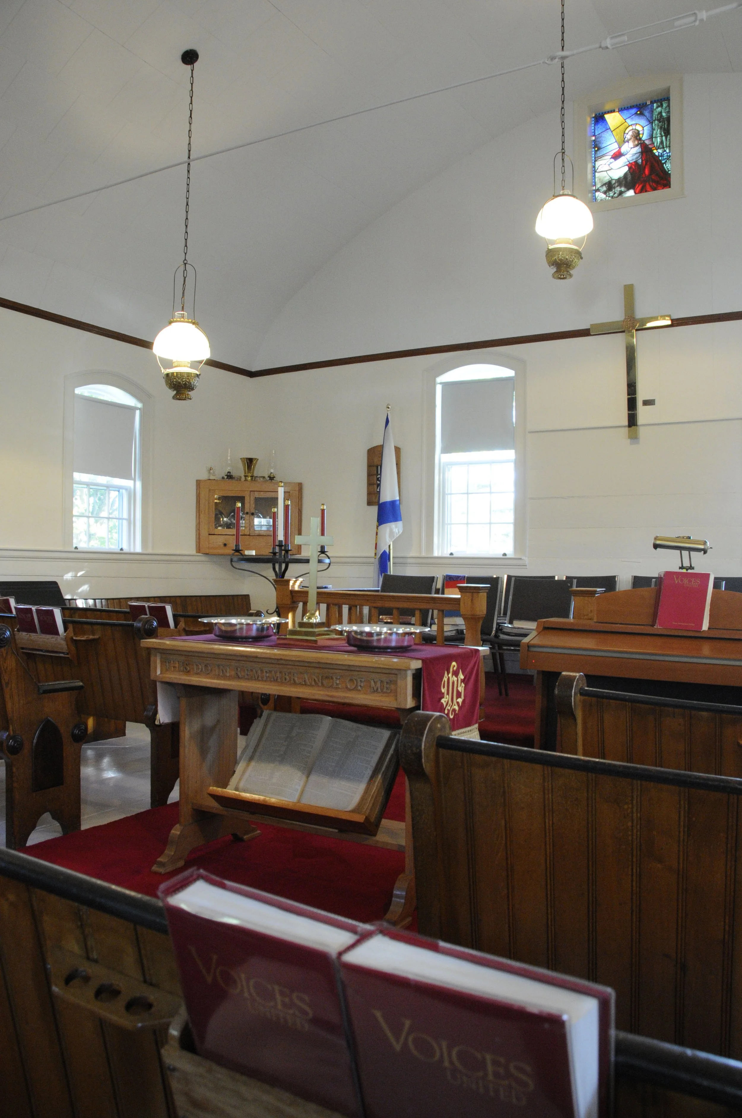 The interior of William Black Memorial United Church showing a bright interior with an arched ceiling. Wood pews, red carpeting and a modest wood communion table decorated with a crimson runner and small brass cross.