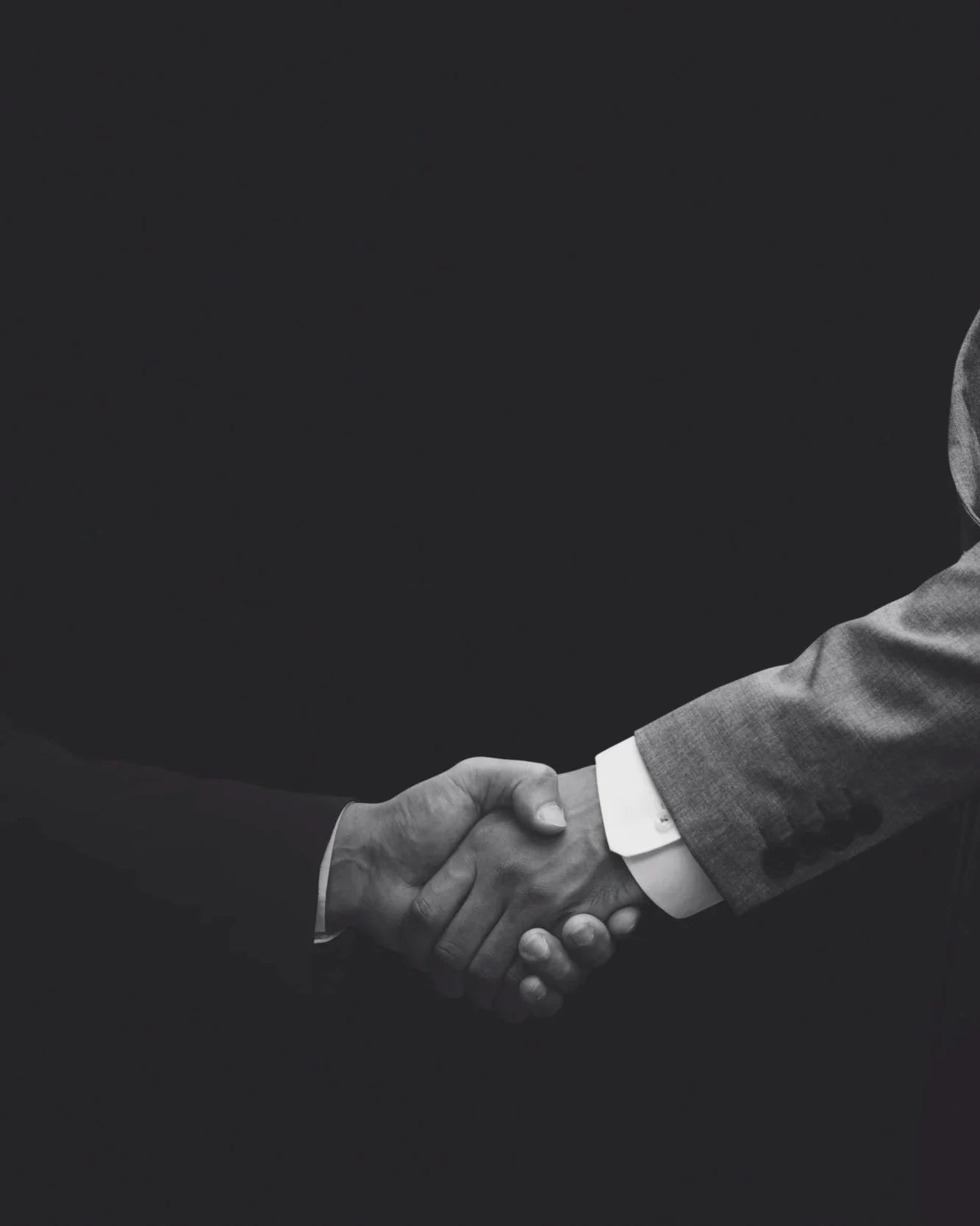 Black and white image of two people shaking hands, one wearing a suit with a visible dress shirt cuff.