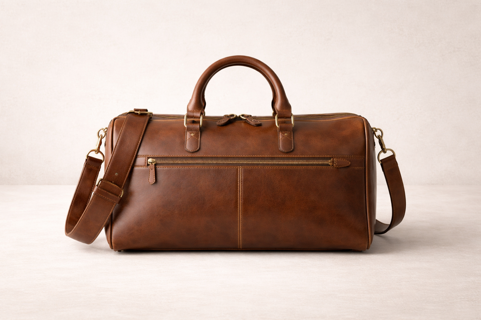 brown leather duffel bag with handles and shoulder strap on a light-colored surface.