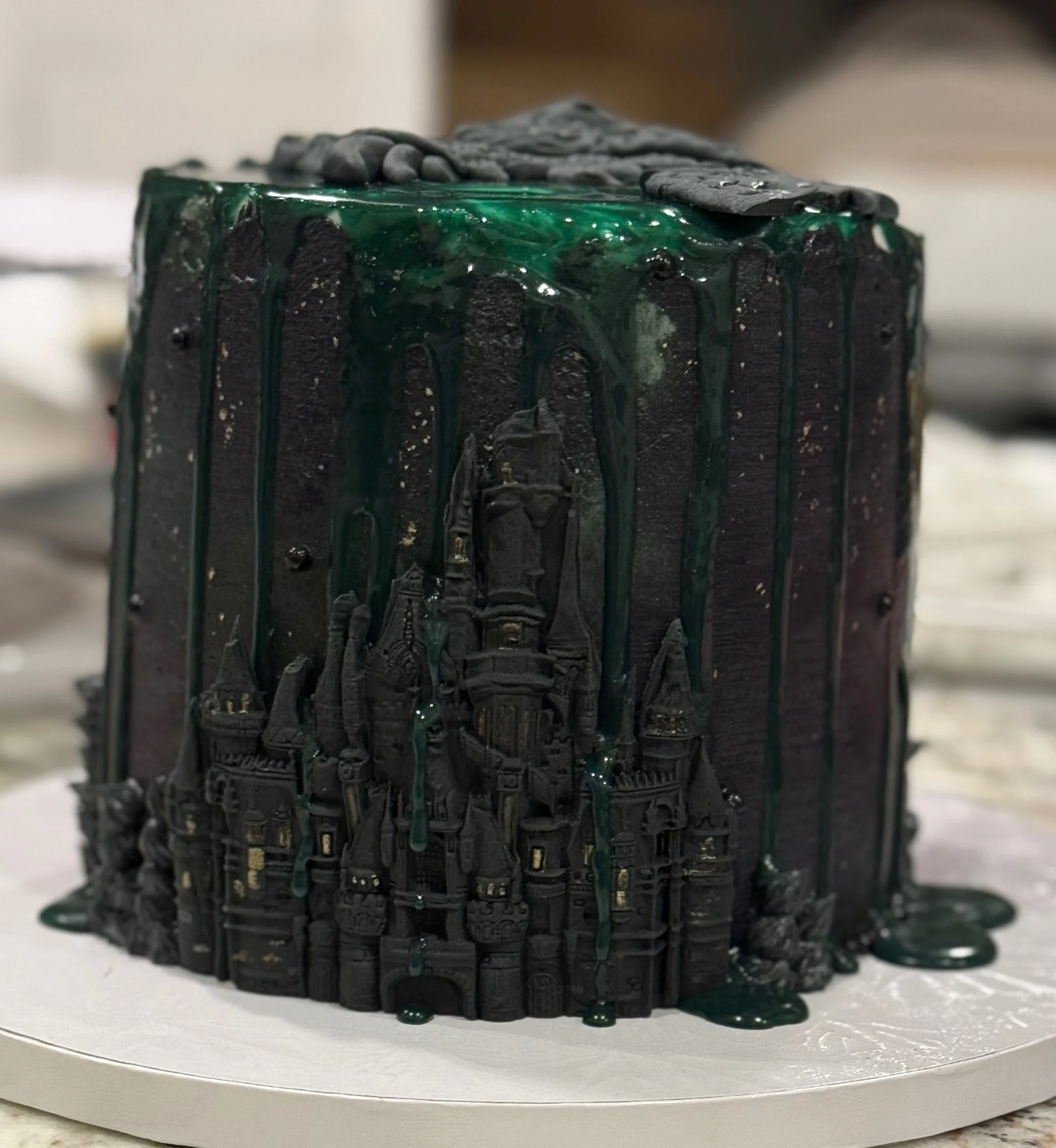A black candle with intricate carvings of buildings, topped with gray stones, with green wax drips down the sides.