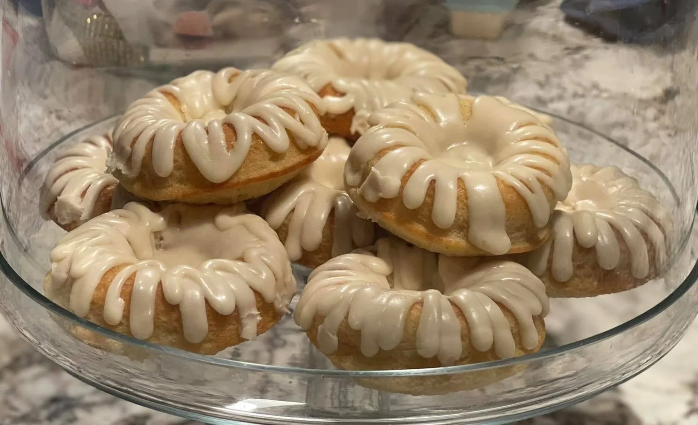 A glass bowl filled with decorated donuts that have white icing drizzled on top.