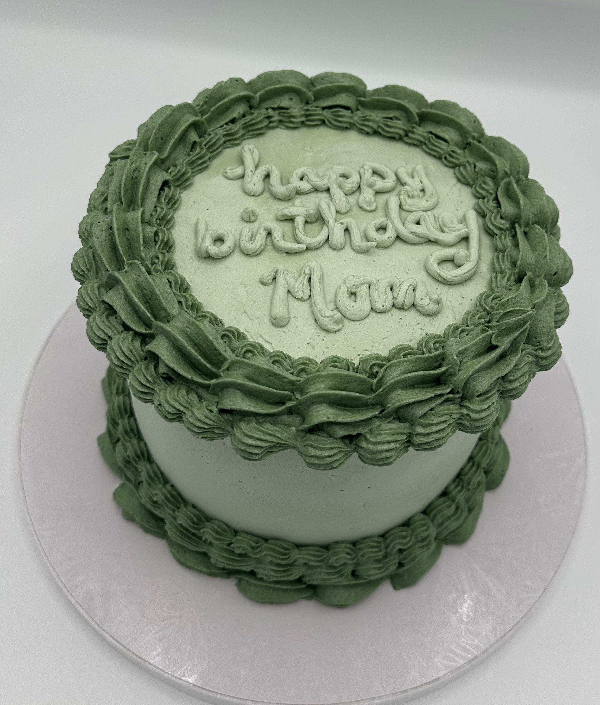 A round cake decorated with green frosting, featuring a piped border and a happy birthday message on top.