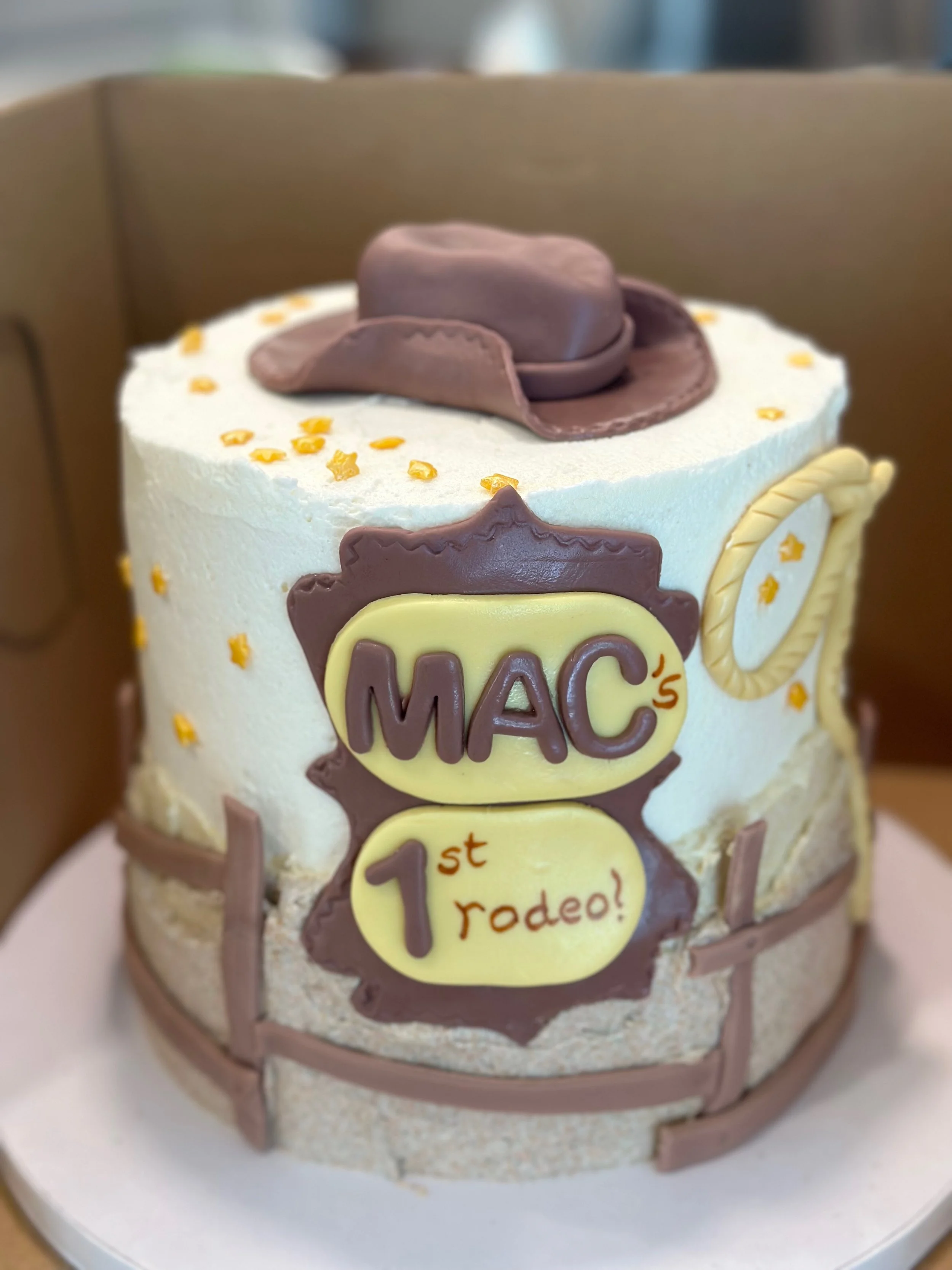 A cake decorated with a sheriff's hat, sheriff badge, and the words 'Mac 1st rodeo!' indicating a first birthday celebration themed around cowboy or sheriff motifs.