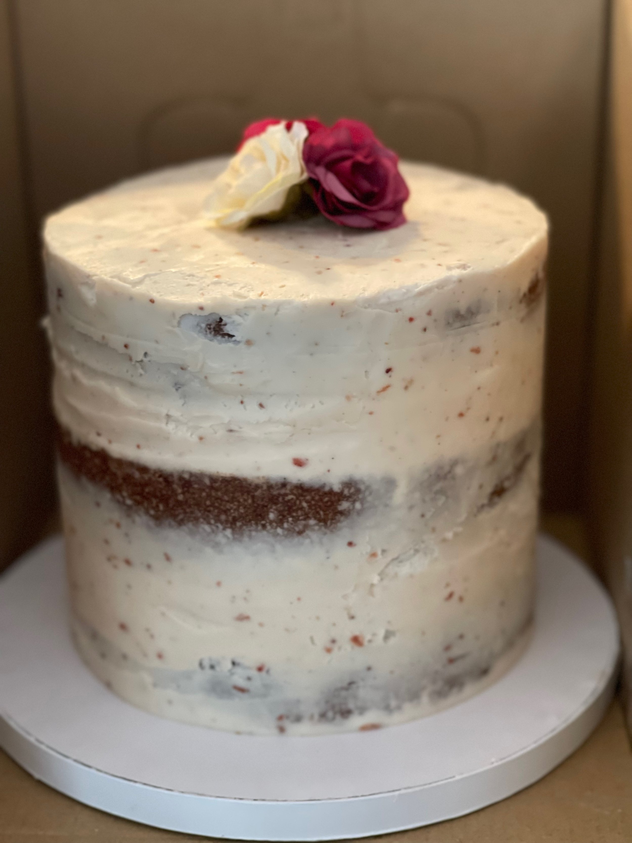 Close-up of a birthday cake with white frosting, decorated with a pink and white rose on top, inside a box.