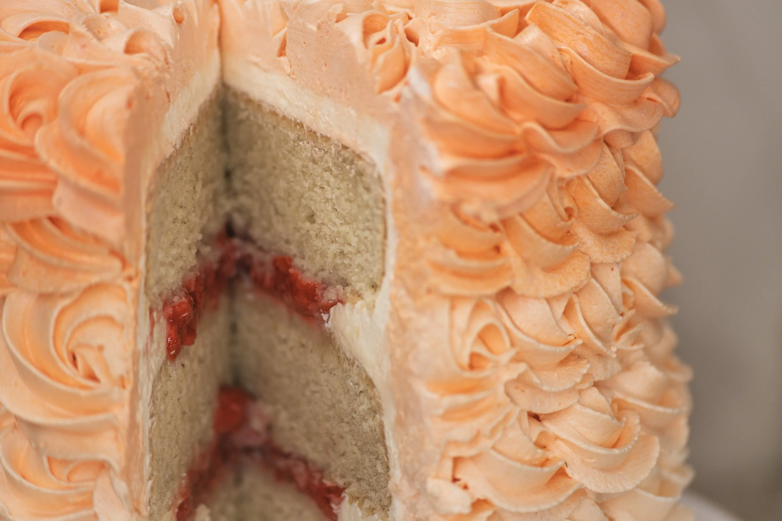 A close-up of a decorated cake with orange colored frosting and ruffled piping design, with a section cut to reveal layered interior with filling.