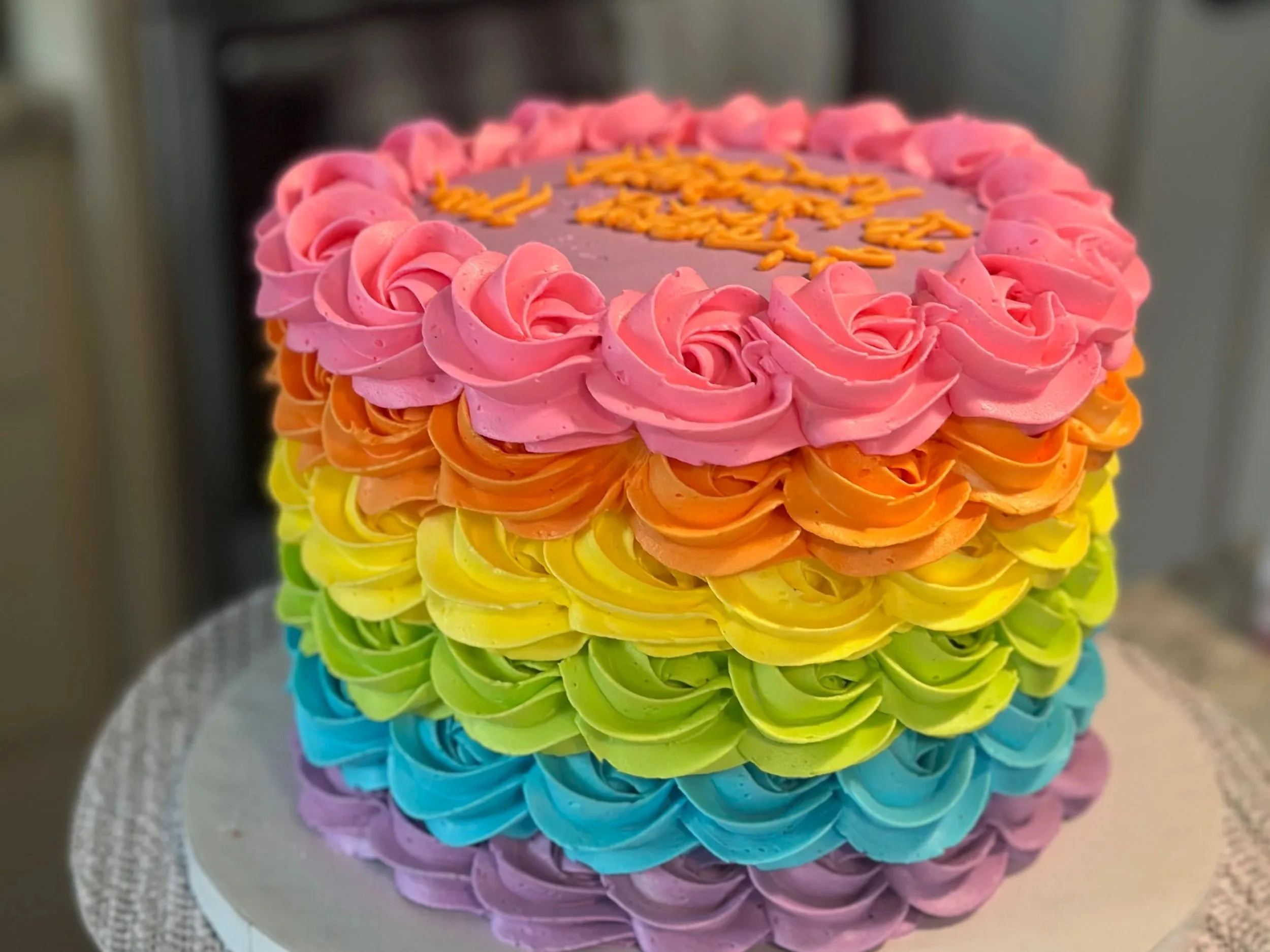 A colorful cake with rainbow-colored frosting arranged in swirls from purple at the bottom to pink at the top.