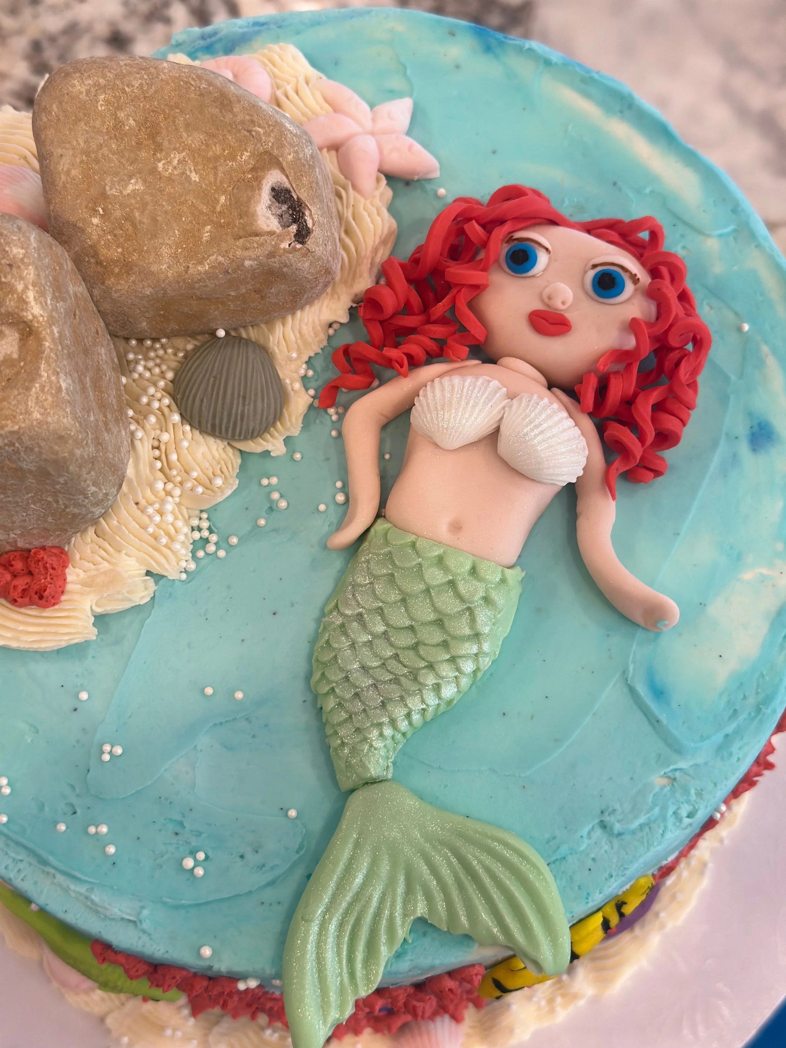 Cake decorated with a mermaid figure , seashells, coral, and ocean-inspired decorations.
