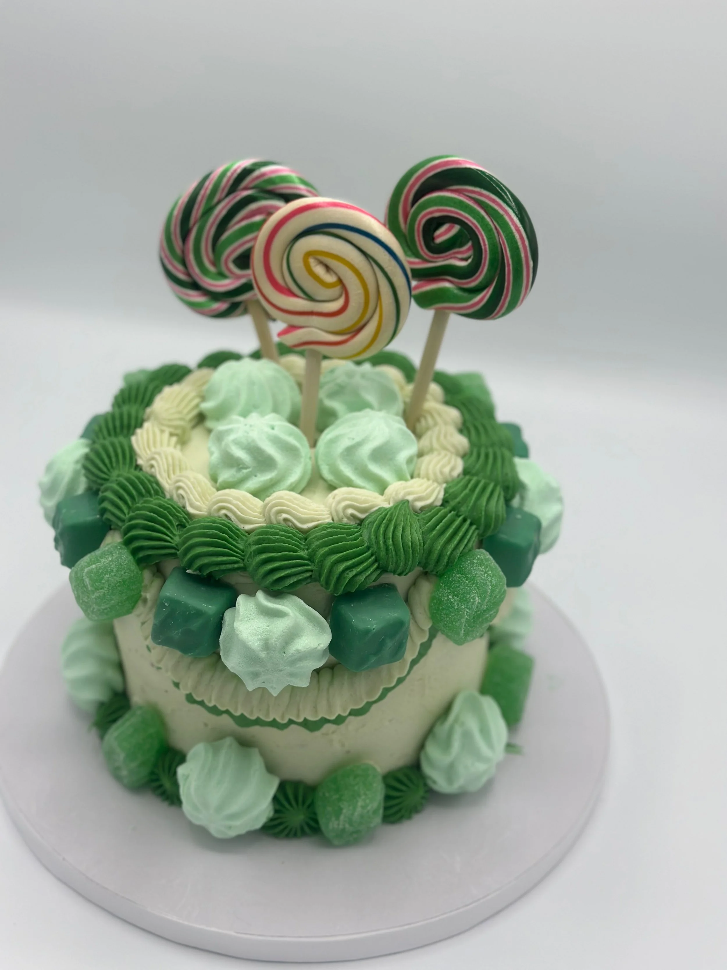 Cake decorated with green and white frosting, topped with colorful peppermint swirl lollipops and candies.