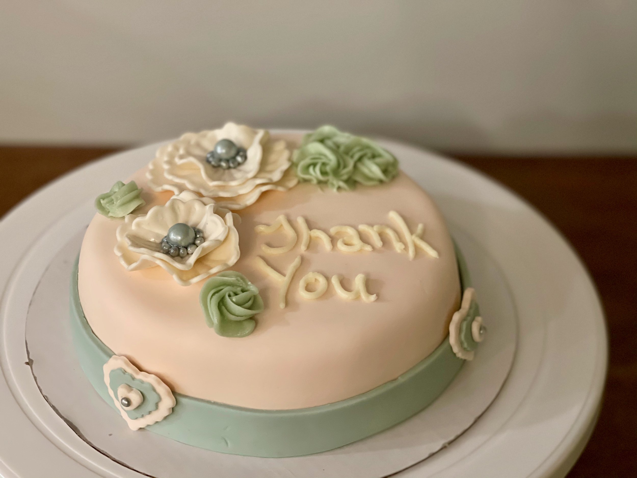 A birthday cake decorated with white and green frosting, topped with decorative flowers and silver pearls, with some writing on it.
