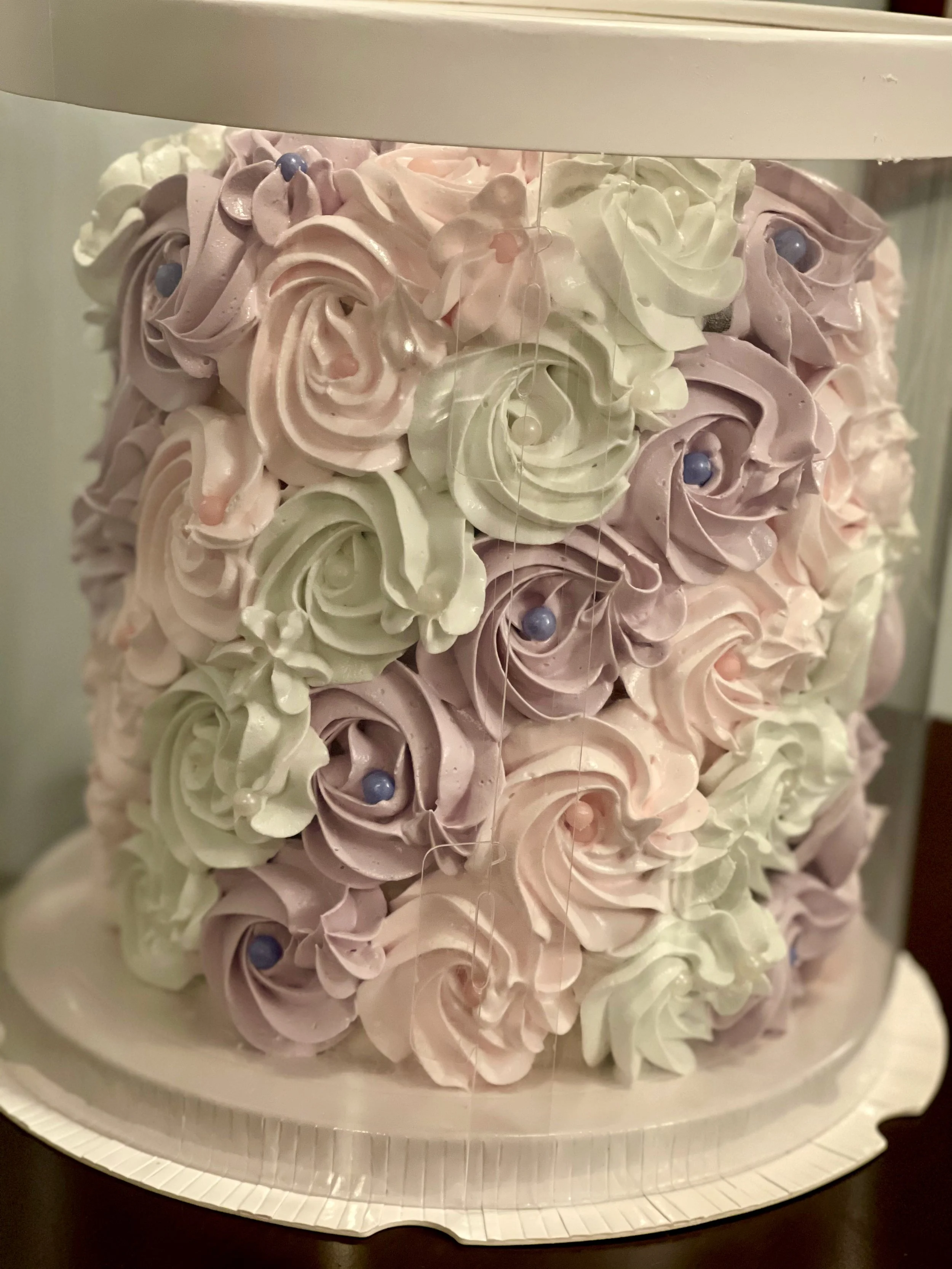A cake decorated with pastel swirl icing in pink and white, topped with edible sugar pearls.