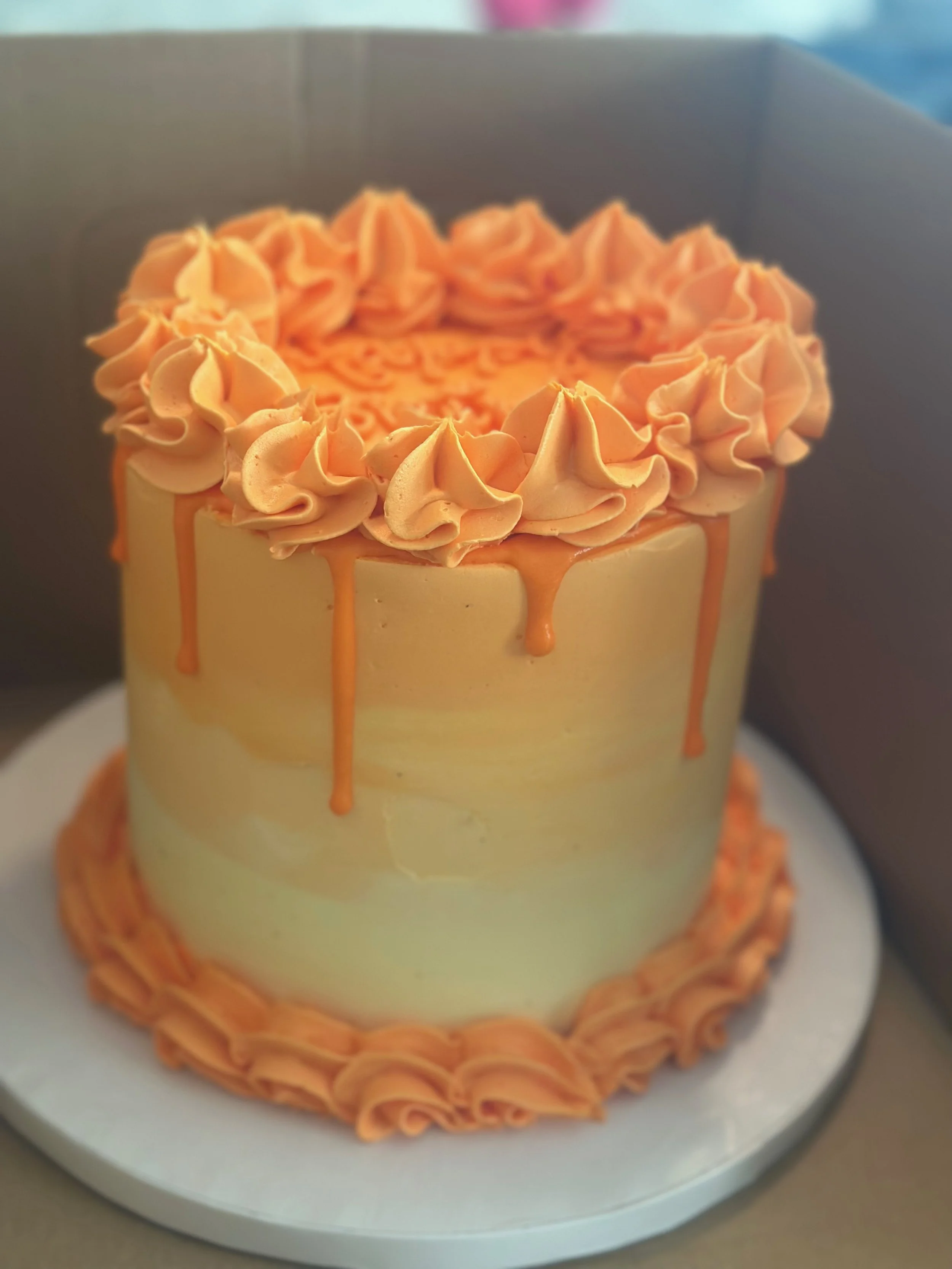 A cake decorated with peach-colored frosting and icing, with a decorative piped border on top and a drippy glaze.