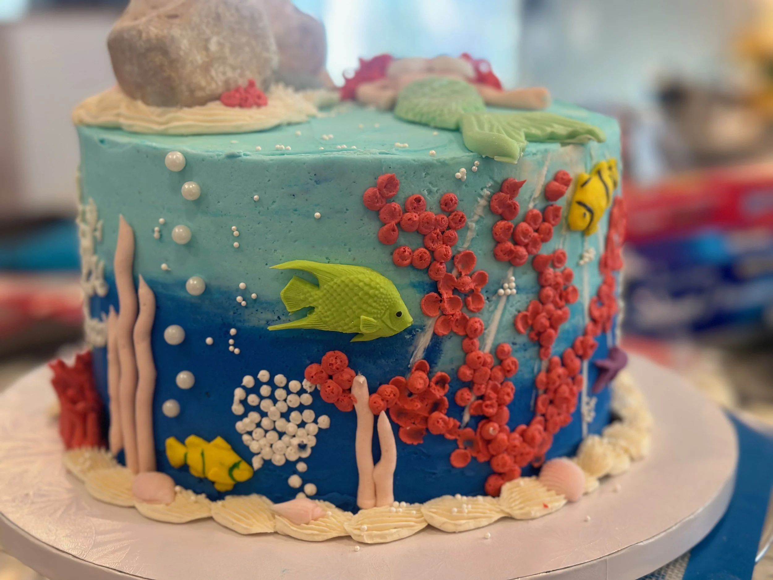 A decorated birthday cake with an underwater/ocean theme, featuring fish, coral, bubbles, and seaweed made of colorful icing.