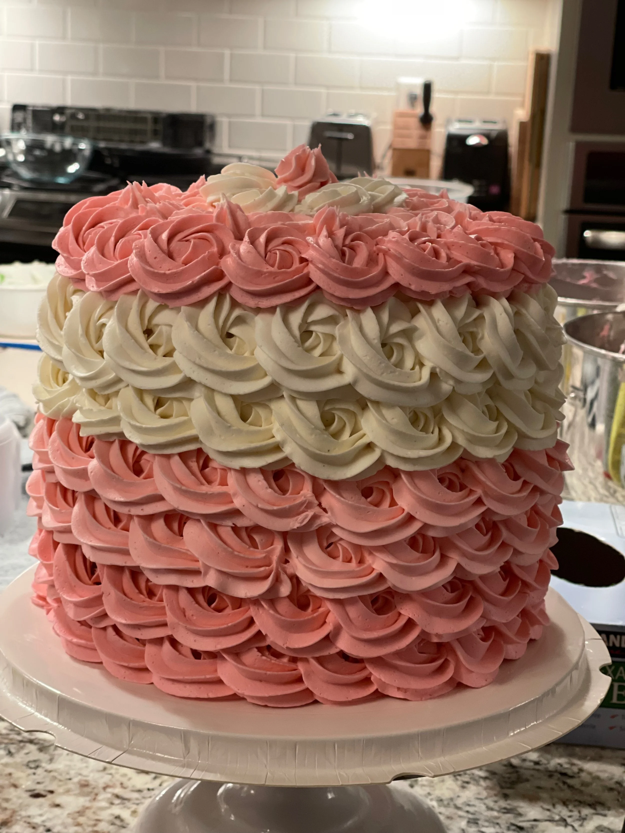 A multi-layer cake decorated with swirled pink and white frosting, displayed on a white cake stand.