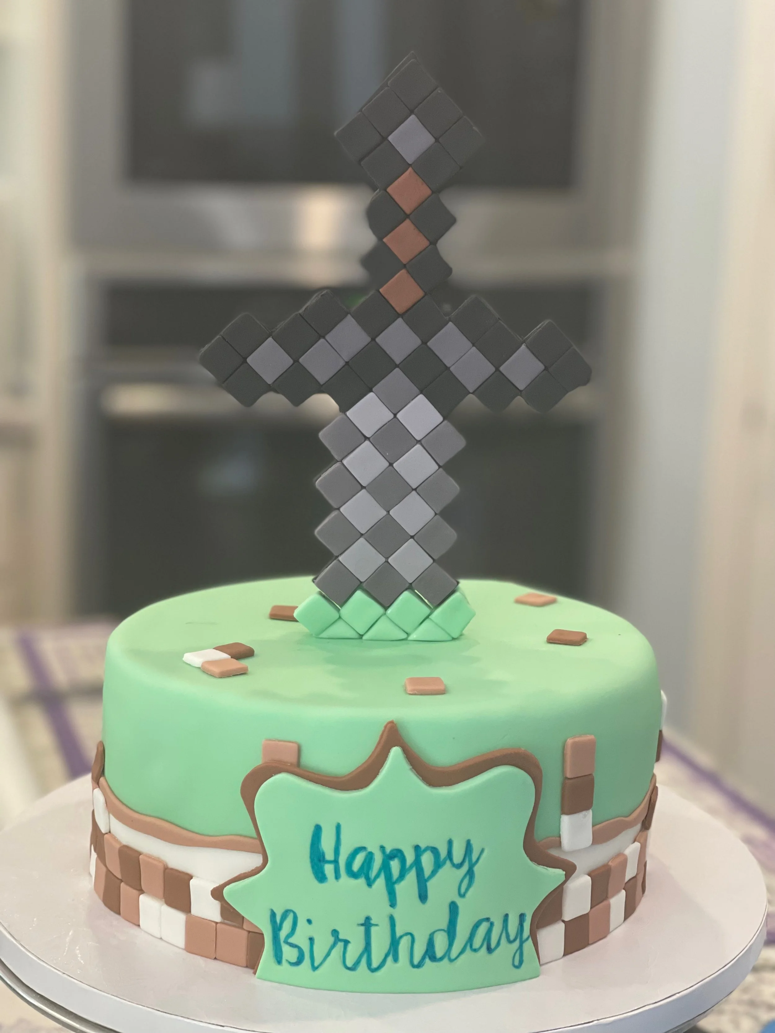 Colorful birthday cake with Minecraft-themed decorations, including a figure resembling a Minecraft sword, green frosting, and a blue sign that reads 'Happy Birthday.'