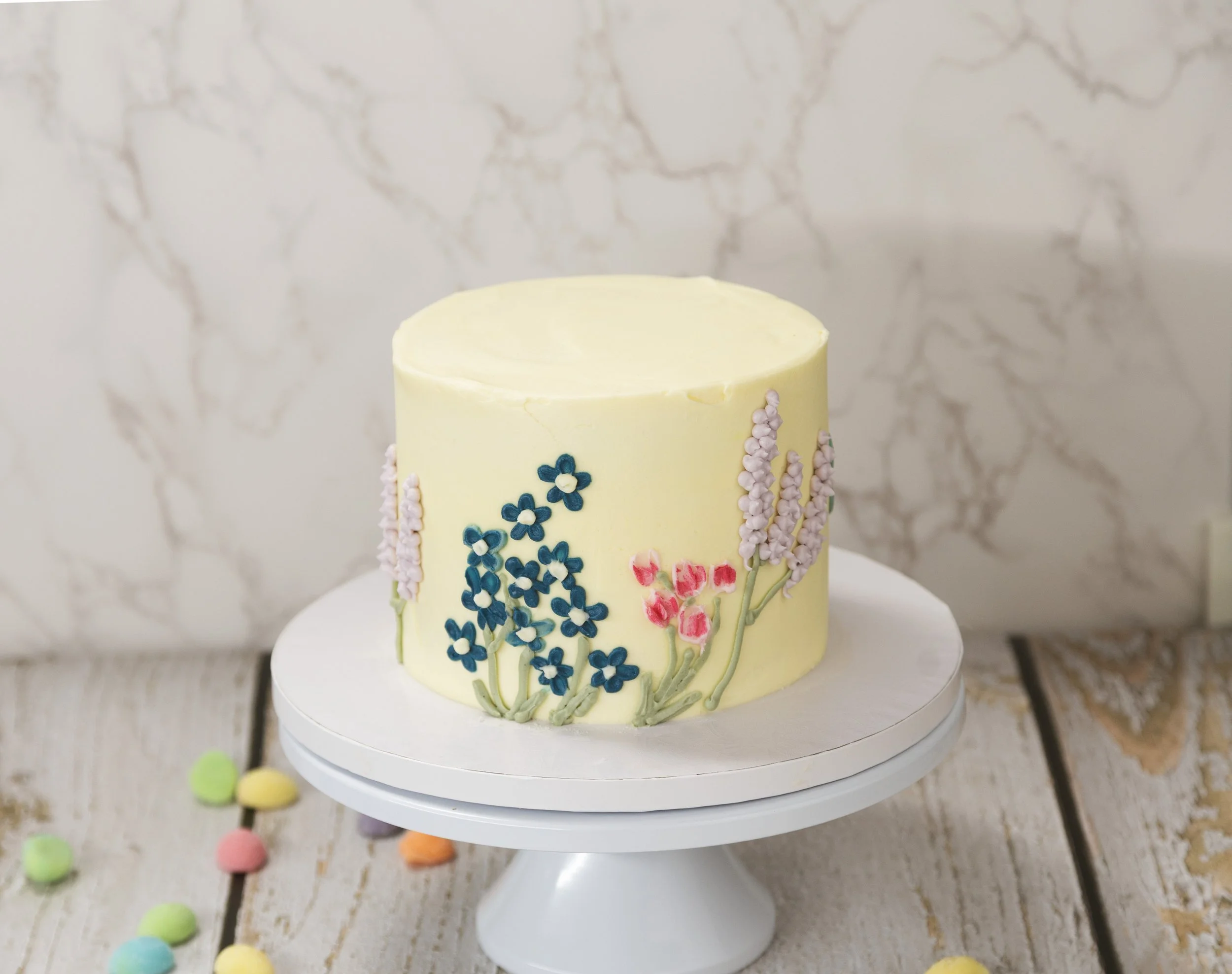Yellow cake decorated with blue and pink floral icing, placed on a white cake stand.