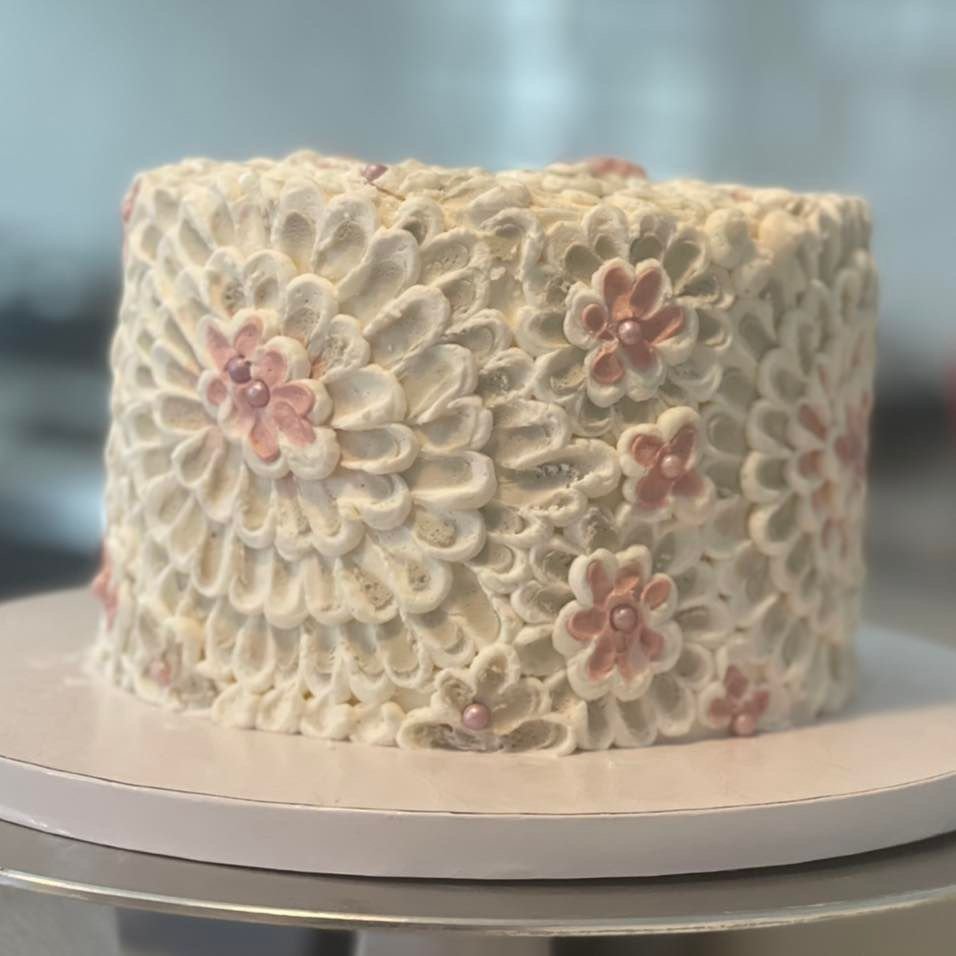 A round cake decorated with white and pink floral icing designs.
