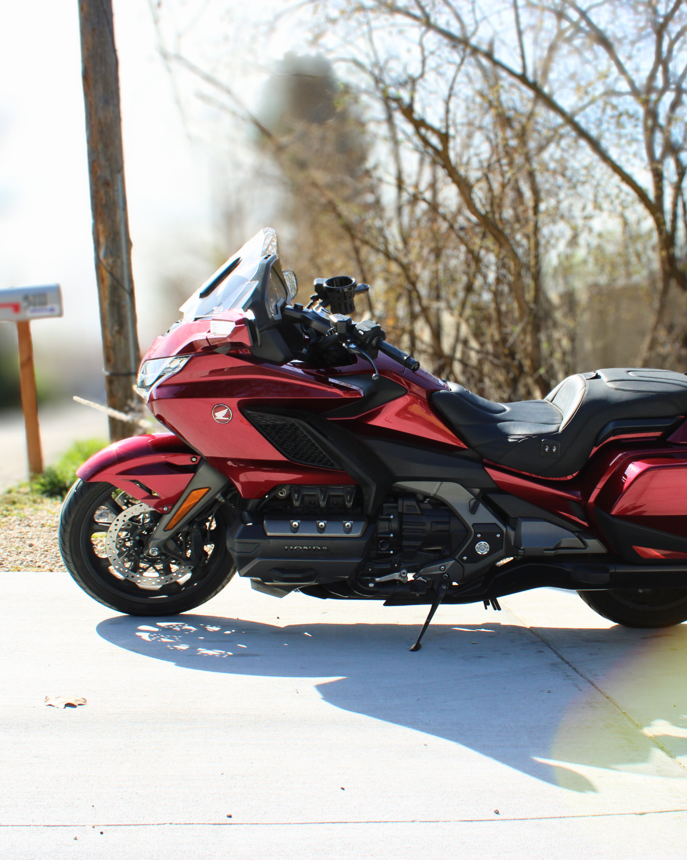Red Honda Gold Wing motorcycle parked on a concrete driveway with trees and a mailbox in the background.